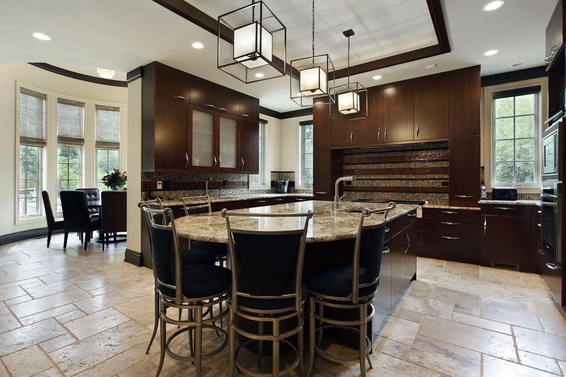A spacious kitchen features dark wood cabinetry, a granite-topped island with metal bar stools, and a mosaic backsplash under cage pendant lights.