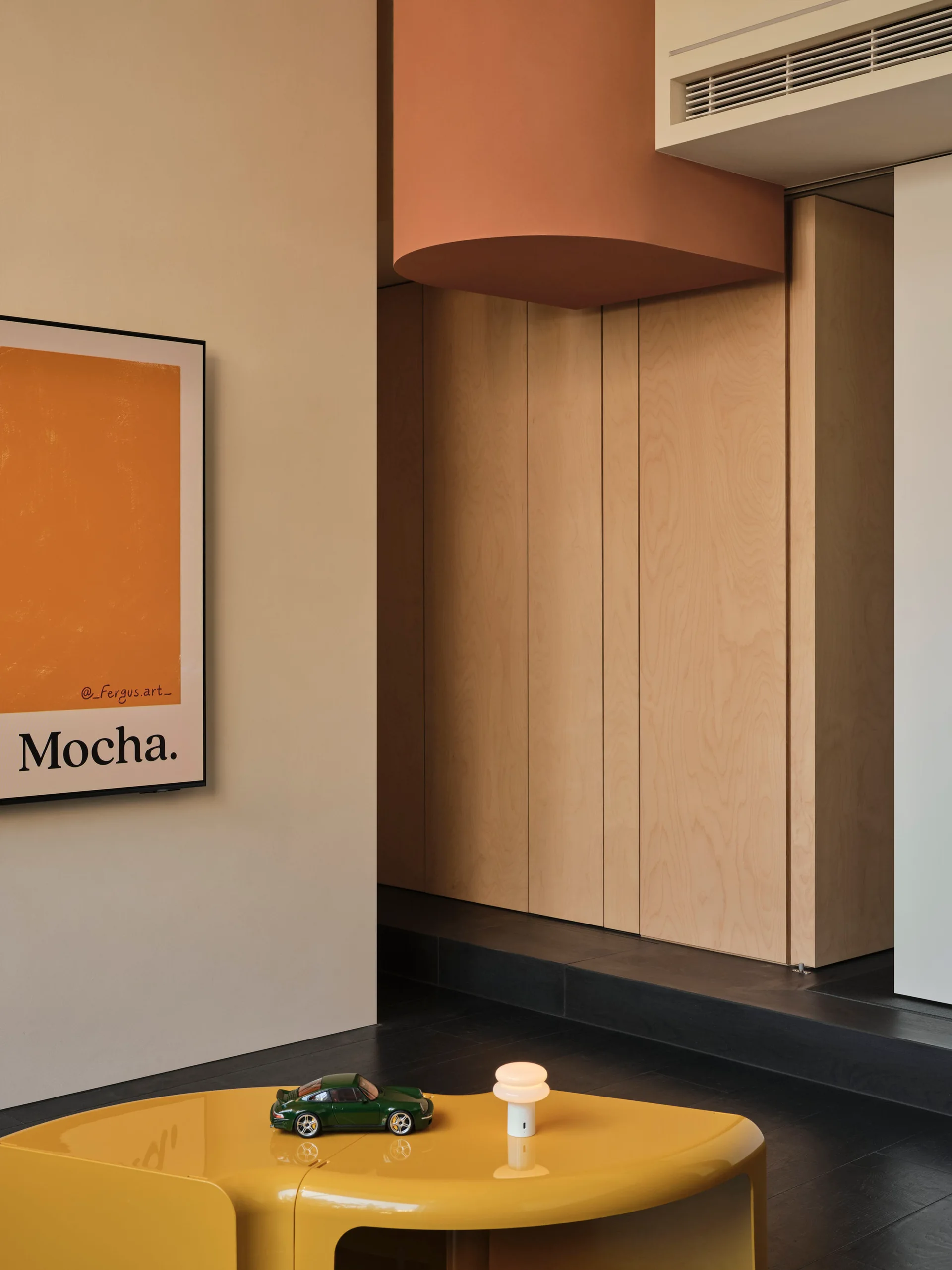 A modern interior corner featuring seamless light wood cabinetry, a curved terracotta ceiling soffit, and a low glossy yellow coffee table.