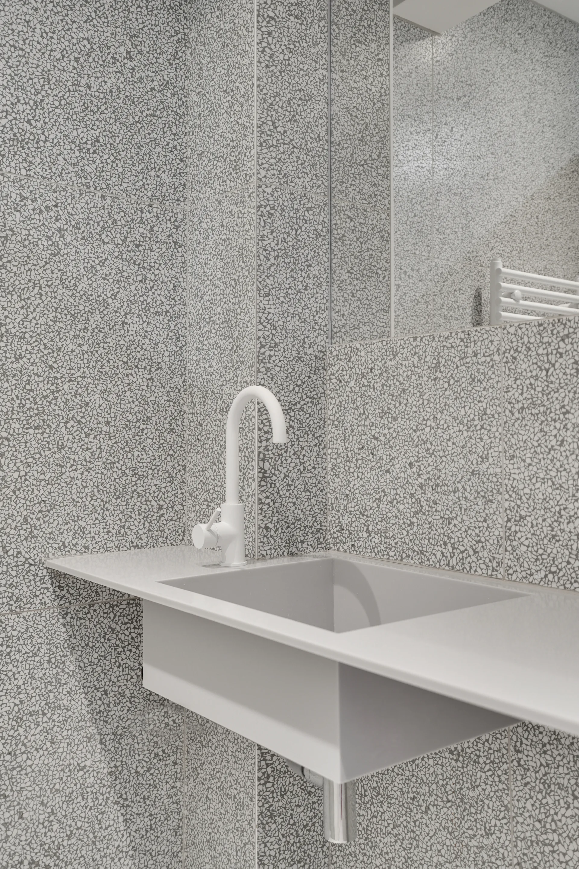 A minimalist grey bathroom vanity sink with an integrated basin, white gooseneck faucet, and grey speckled terrazzo wall tiles.