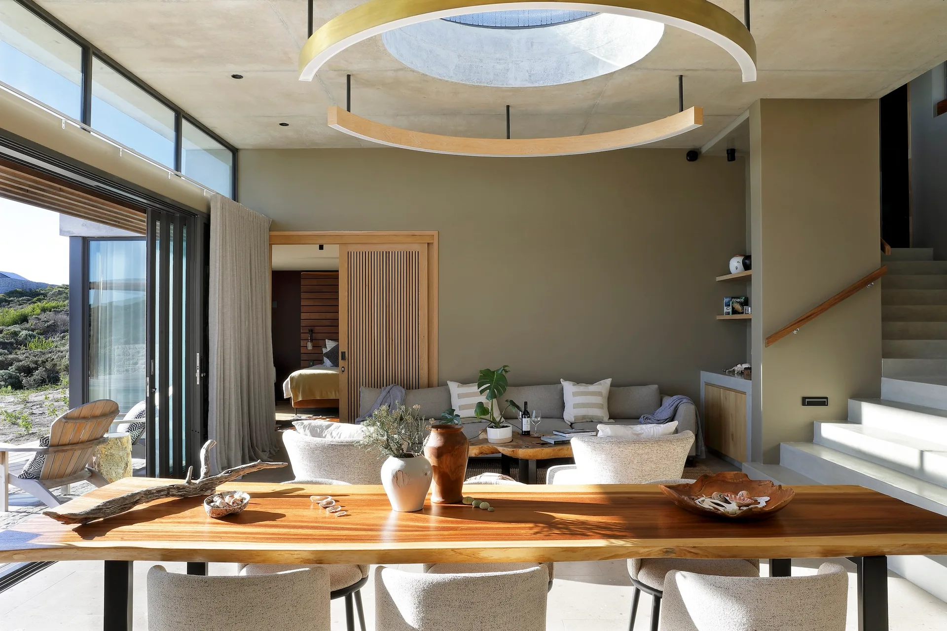 An open-plan living and dining space featuring olive green walls, a live-edge wooden dining table, and a large circular skylight in a concrete ceiling.