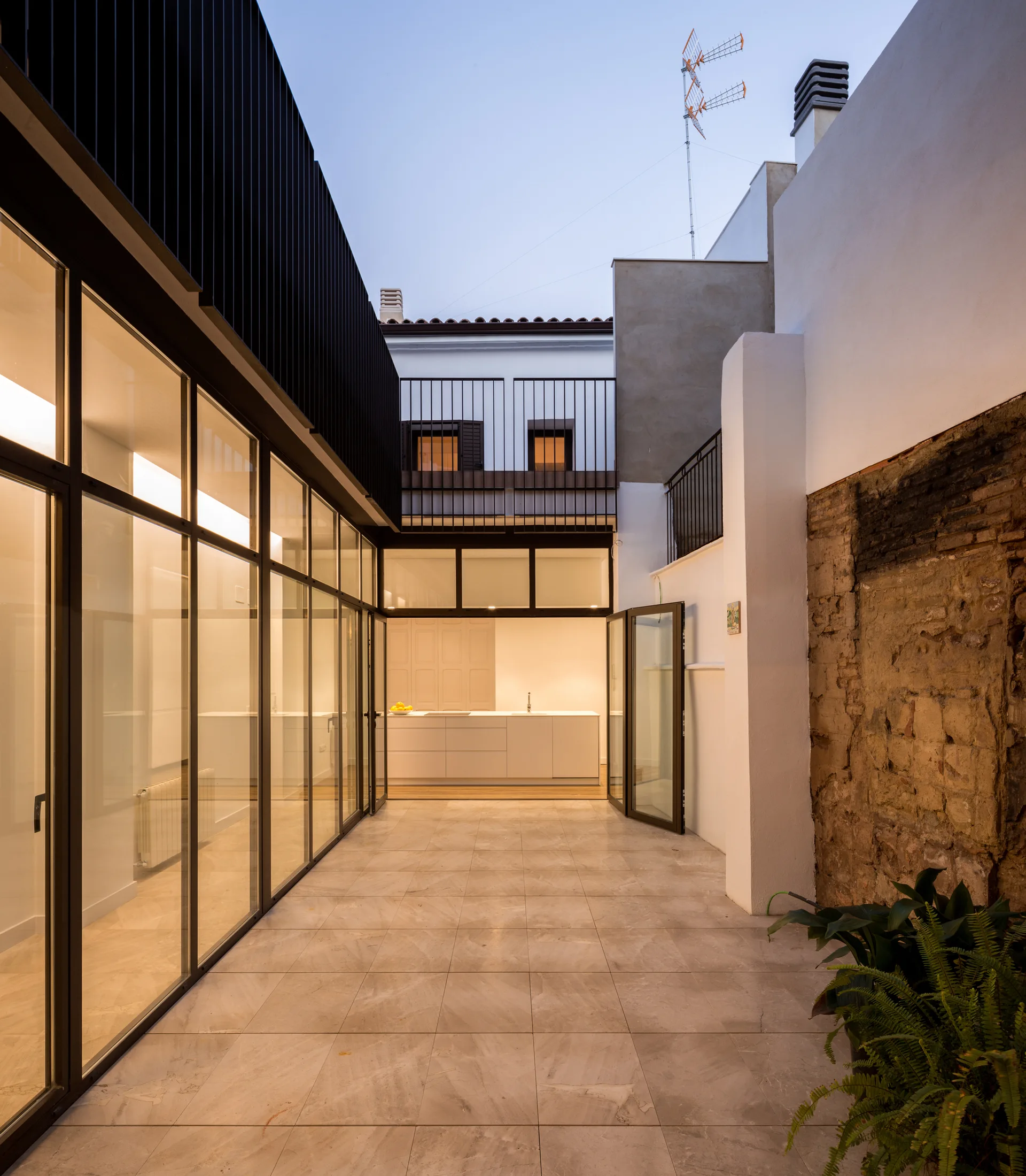 An open-air courtyard with beige stone tile flooring features black-framed glass walls and an exposed brick accent wall.