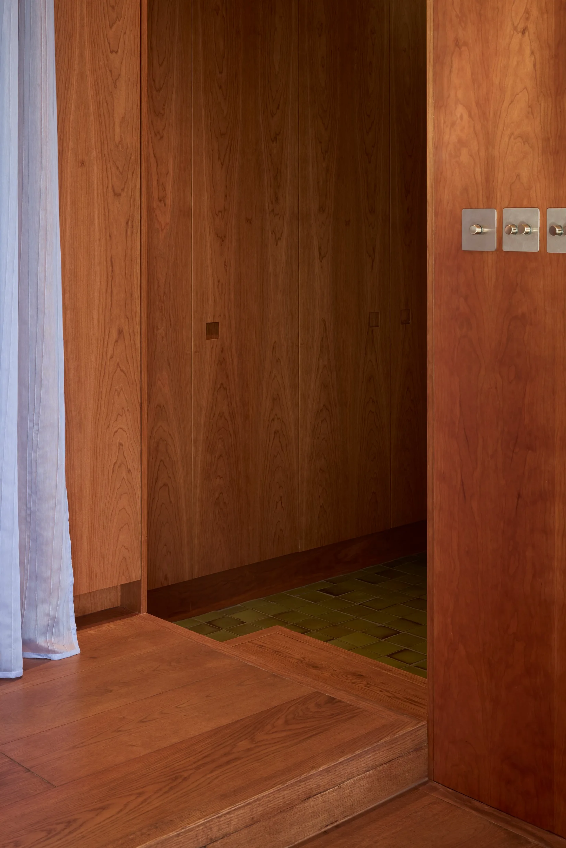 A hallway transition featuring warm wood-paneled walls, wooden flooring, and a step down to green tiled flooring.