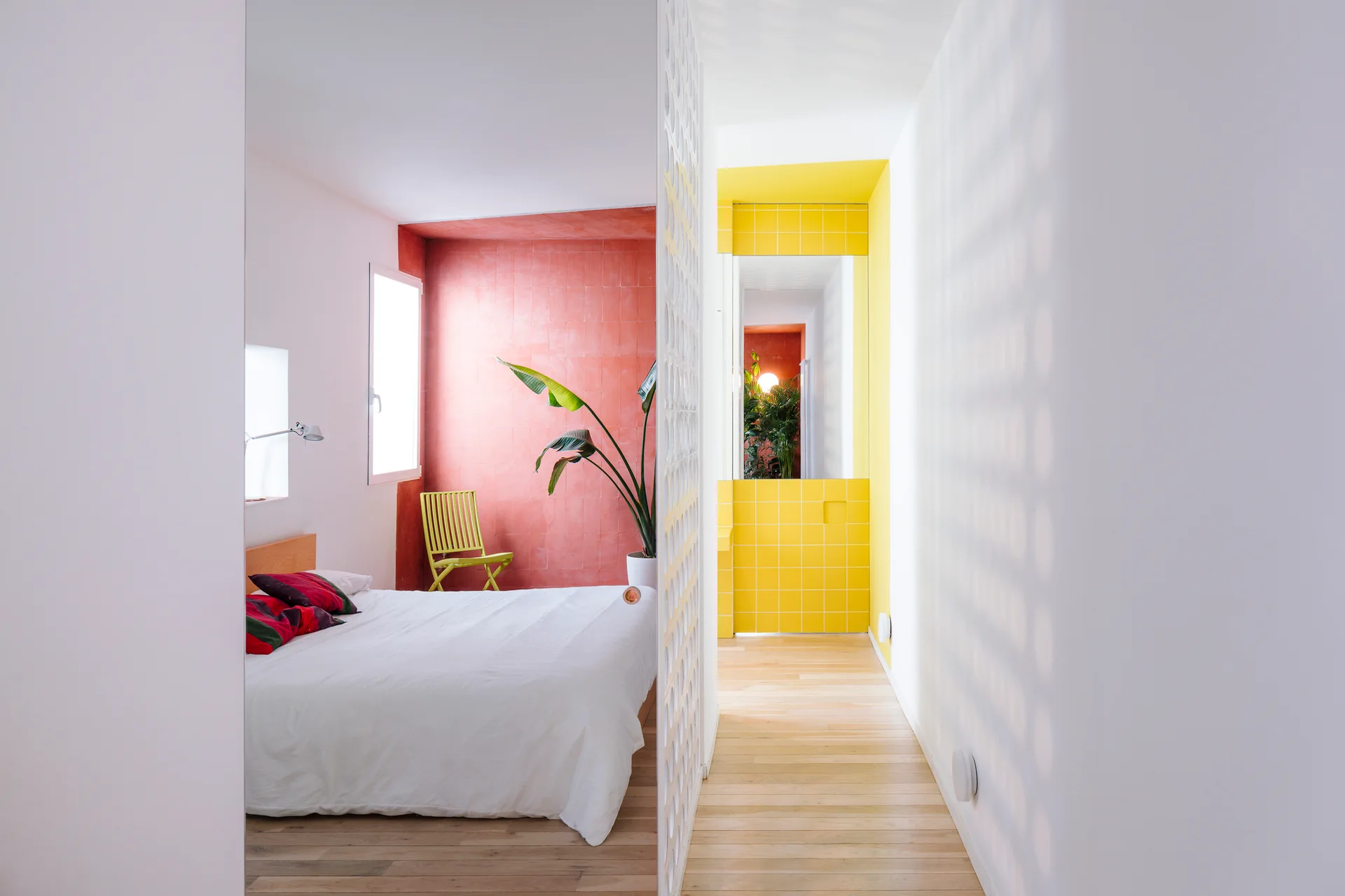 A modern bedroom with a white bed and terracotta accent wall features a white patterned divider screen and a view of a yellow tiled hallway.