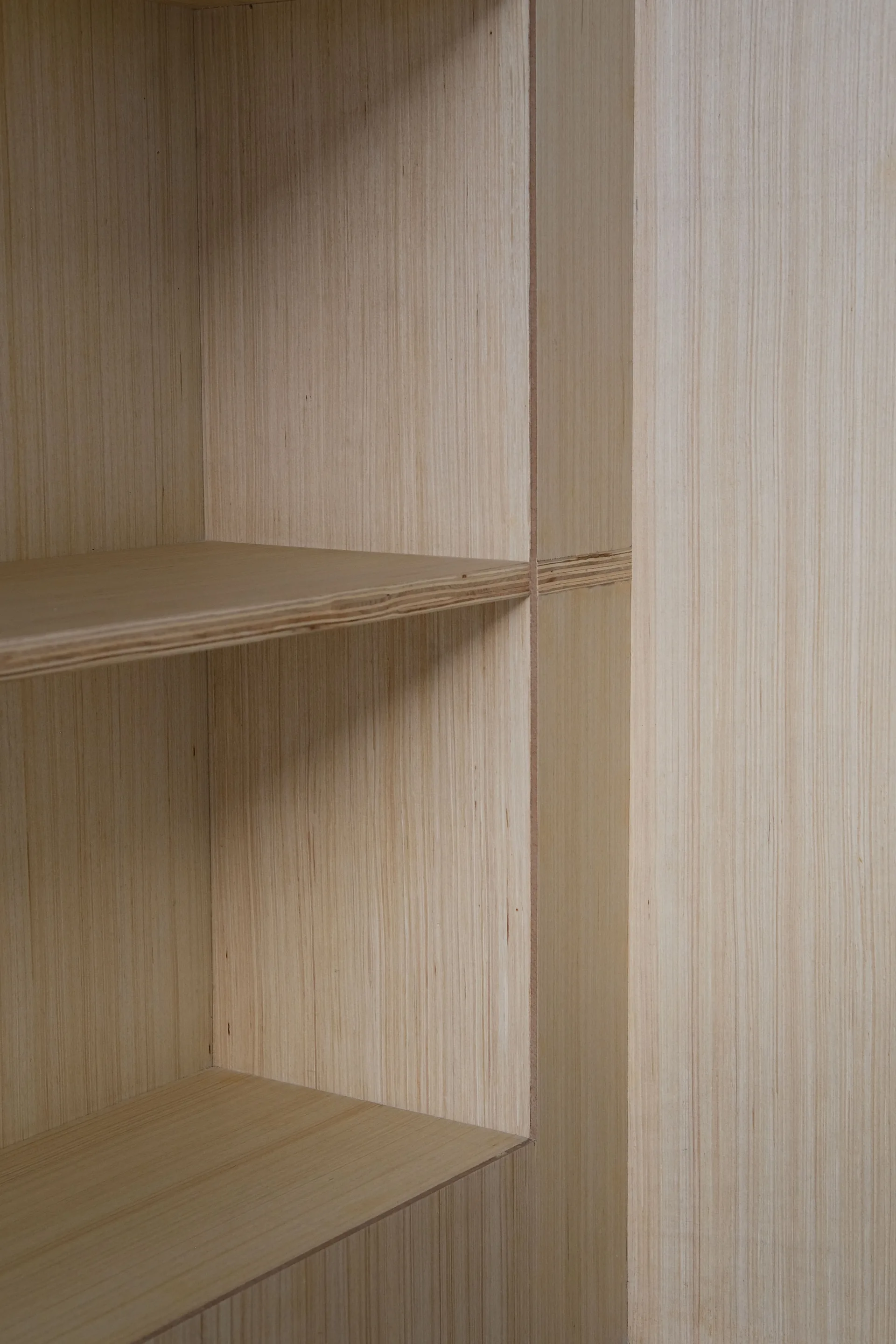 A close-up view of minimalist built-in plywood shelving showing the exposed striped edges and light blonde vertical wood grain.