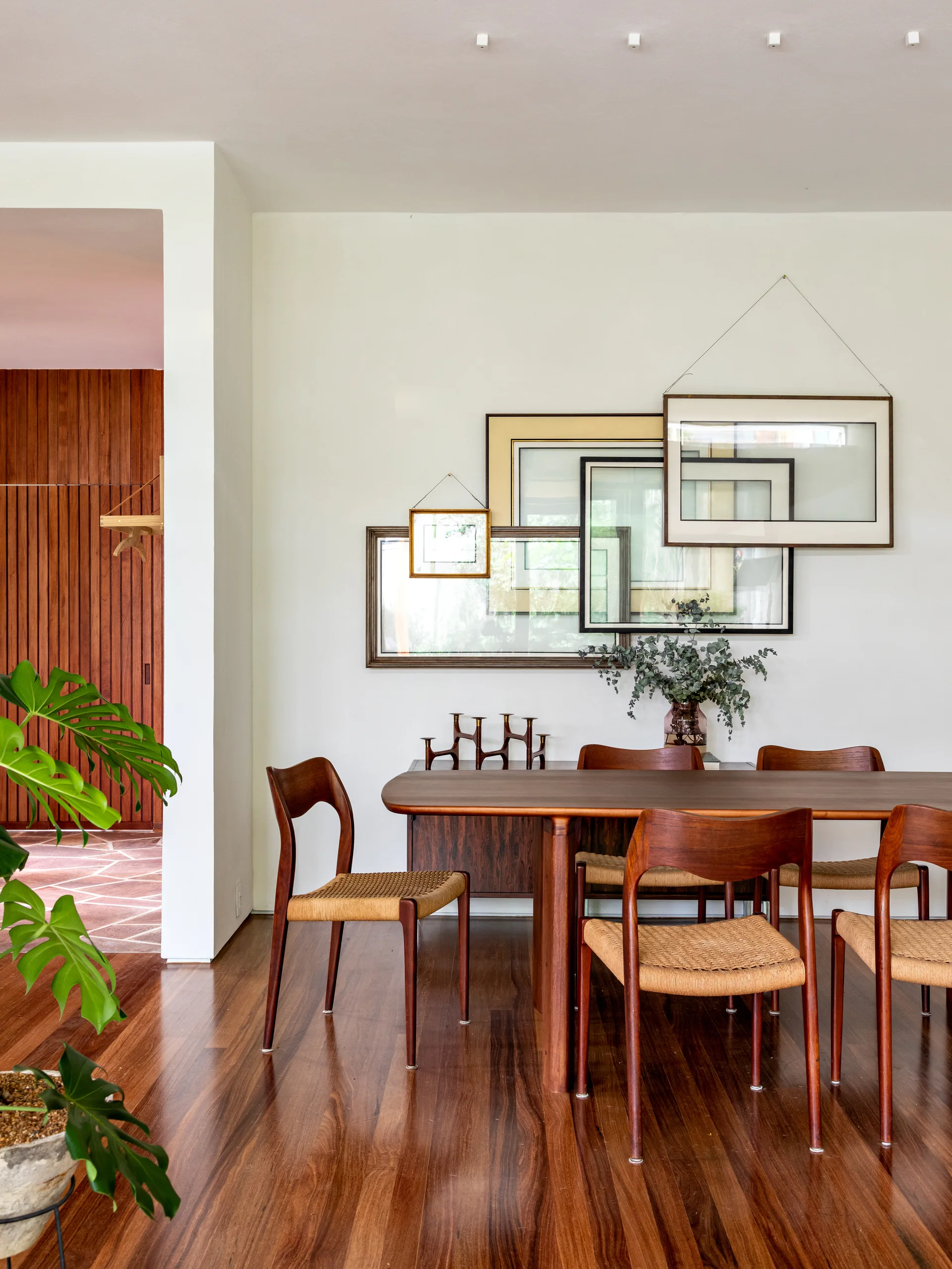 A mid-century modern wood dining set sits in front of a white wall styled with an overlapping gallery of empty wood frames.