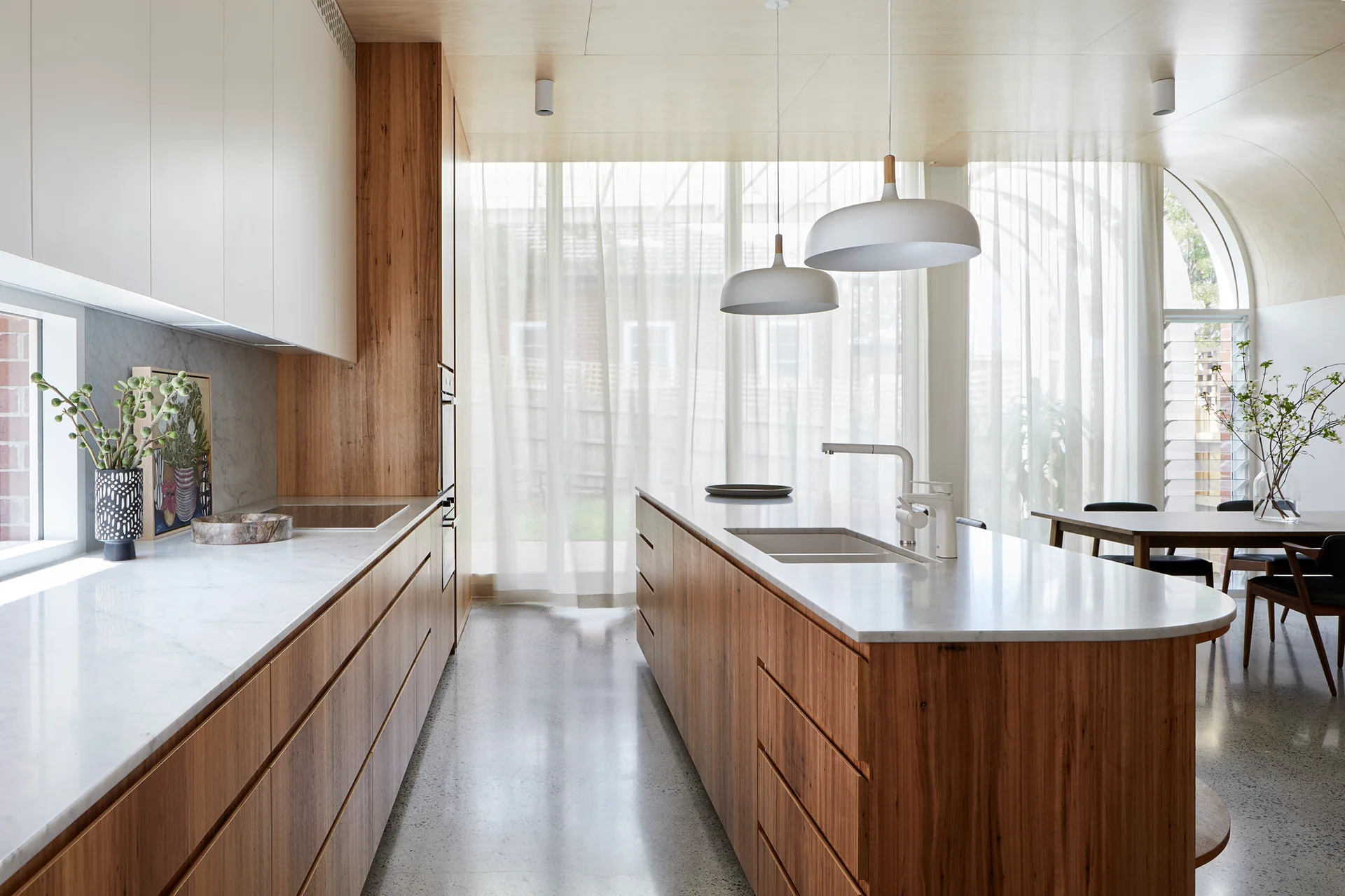 A modern kitchen featuring wood lower cabinetry, white upper cabinets, a large island with a sink, and a polished concrete floor.