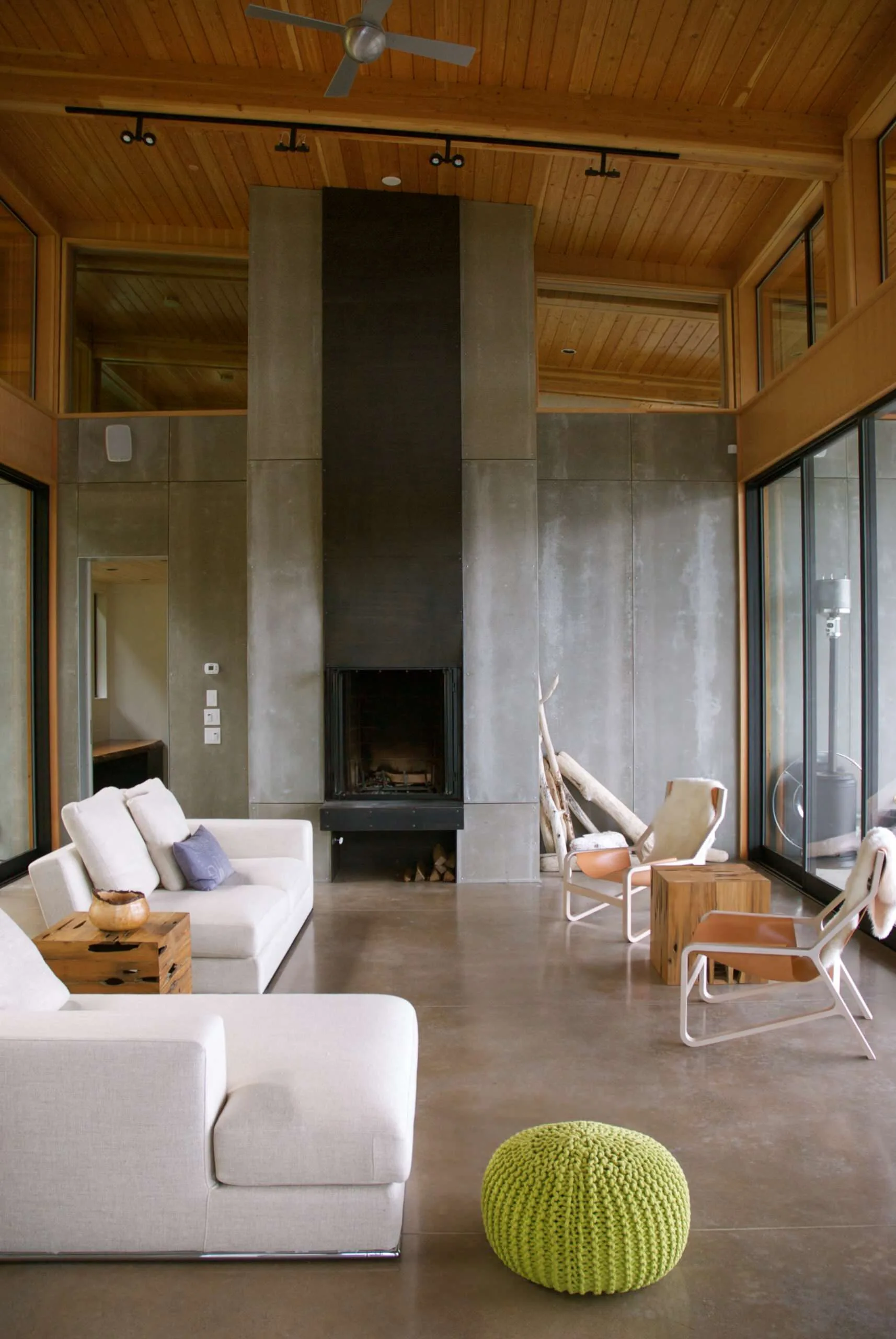 A modern living room featuring a tall concrete panel fireplace, white sofas, wood plank ceilings, and polished concrete floors.