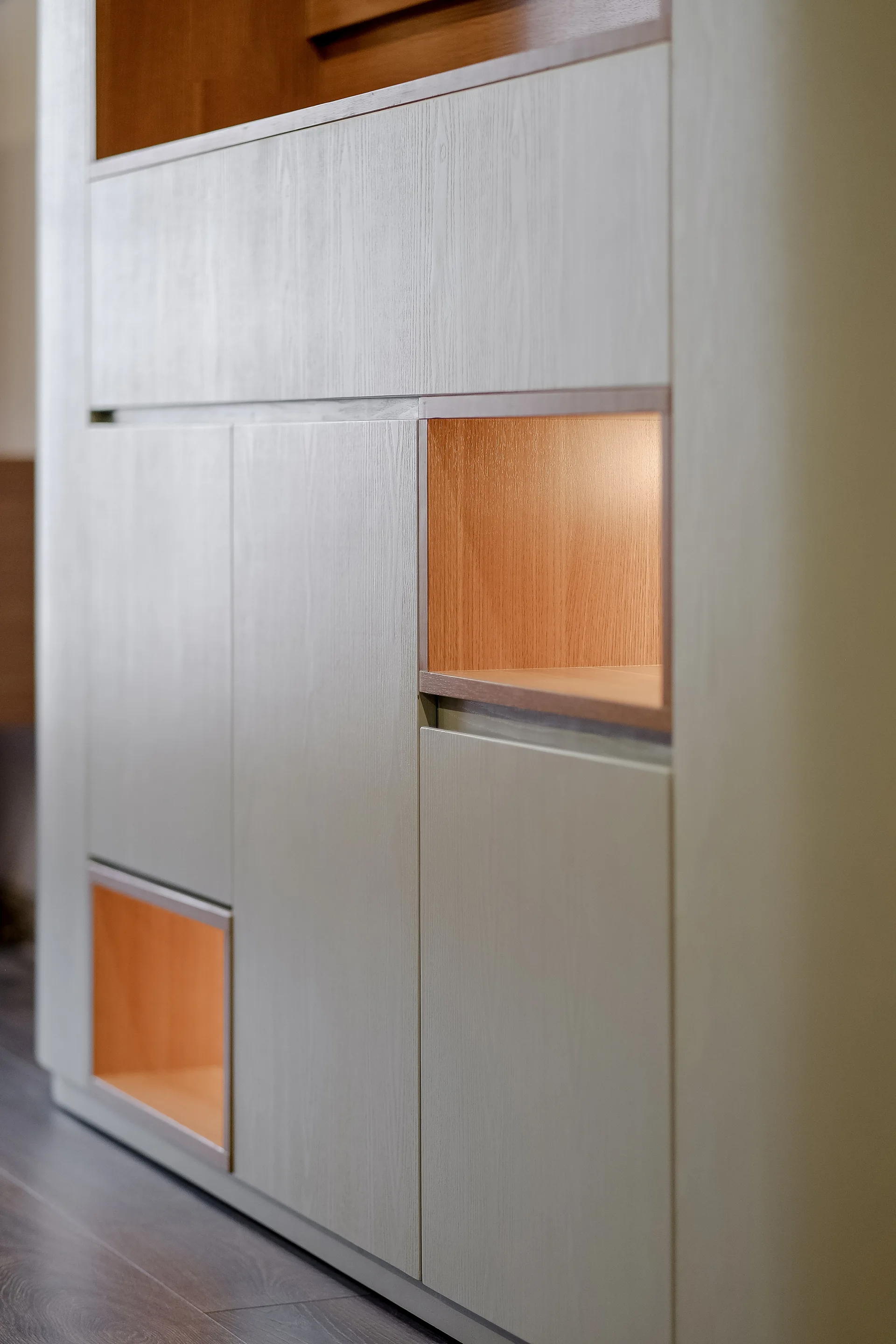 A close-up of light grey custom cabinetry featuring inset wood-toned cubbies with integrated warm lighting.