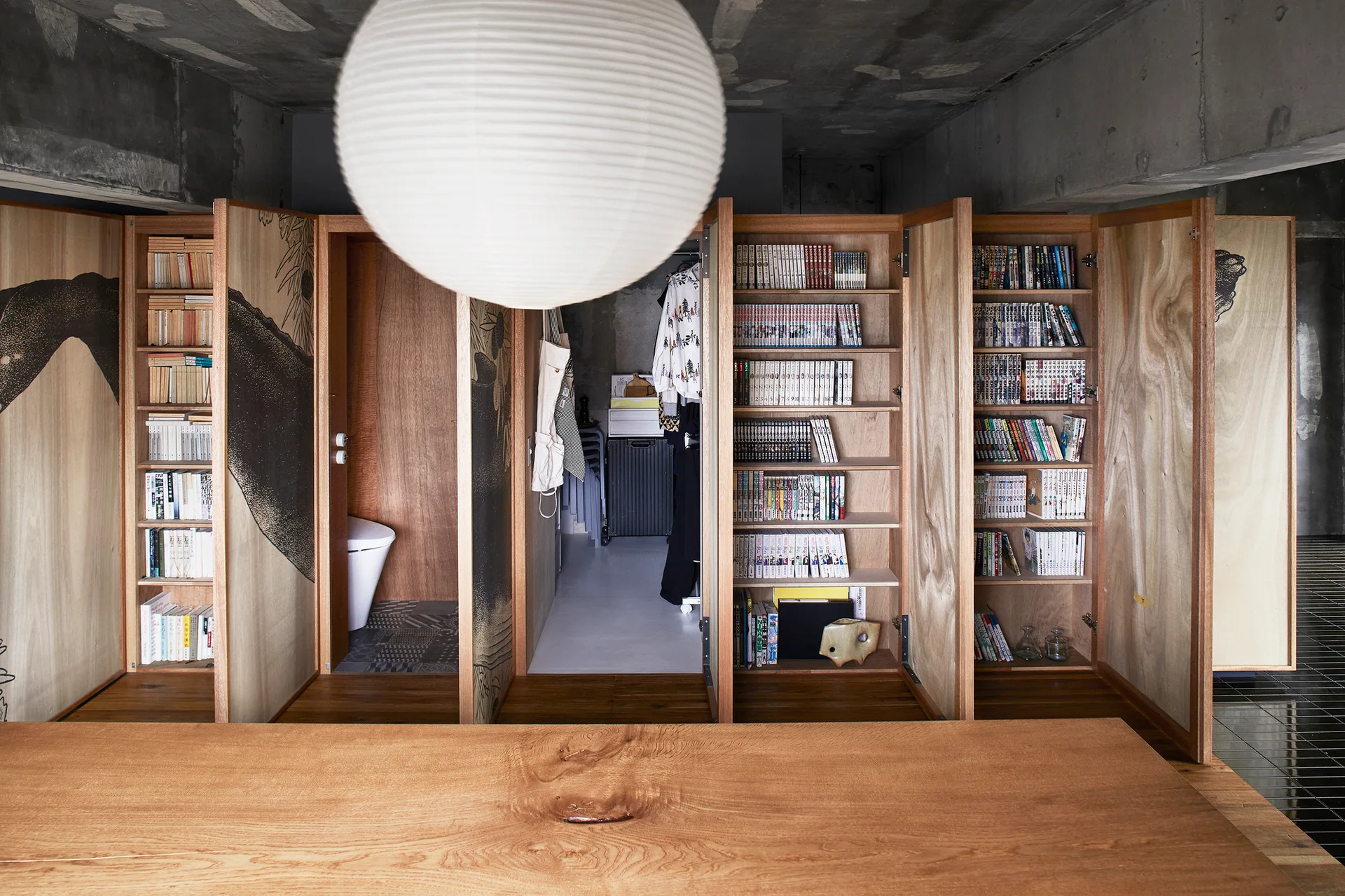 Wooden partition walls with integrated bookshelves stand under an exposed concrete ceiling behind a large wood table.