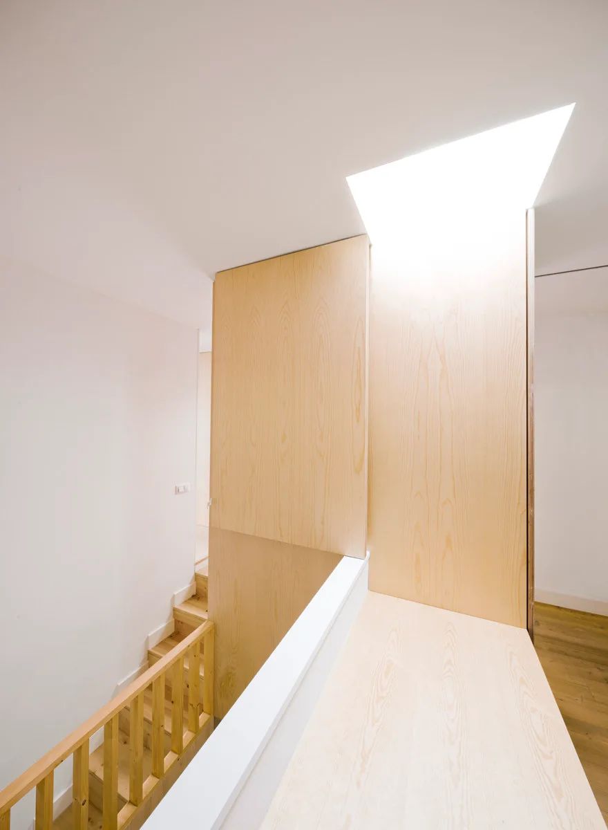 A bright stairwell landing featuring light wood wall panels, a matching wooden railing, and a large skylight in the white ceiling.