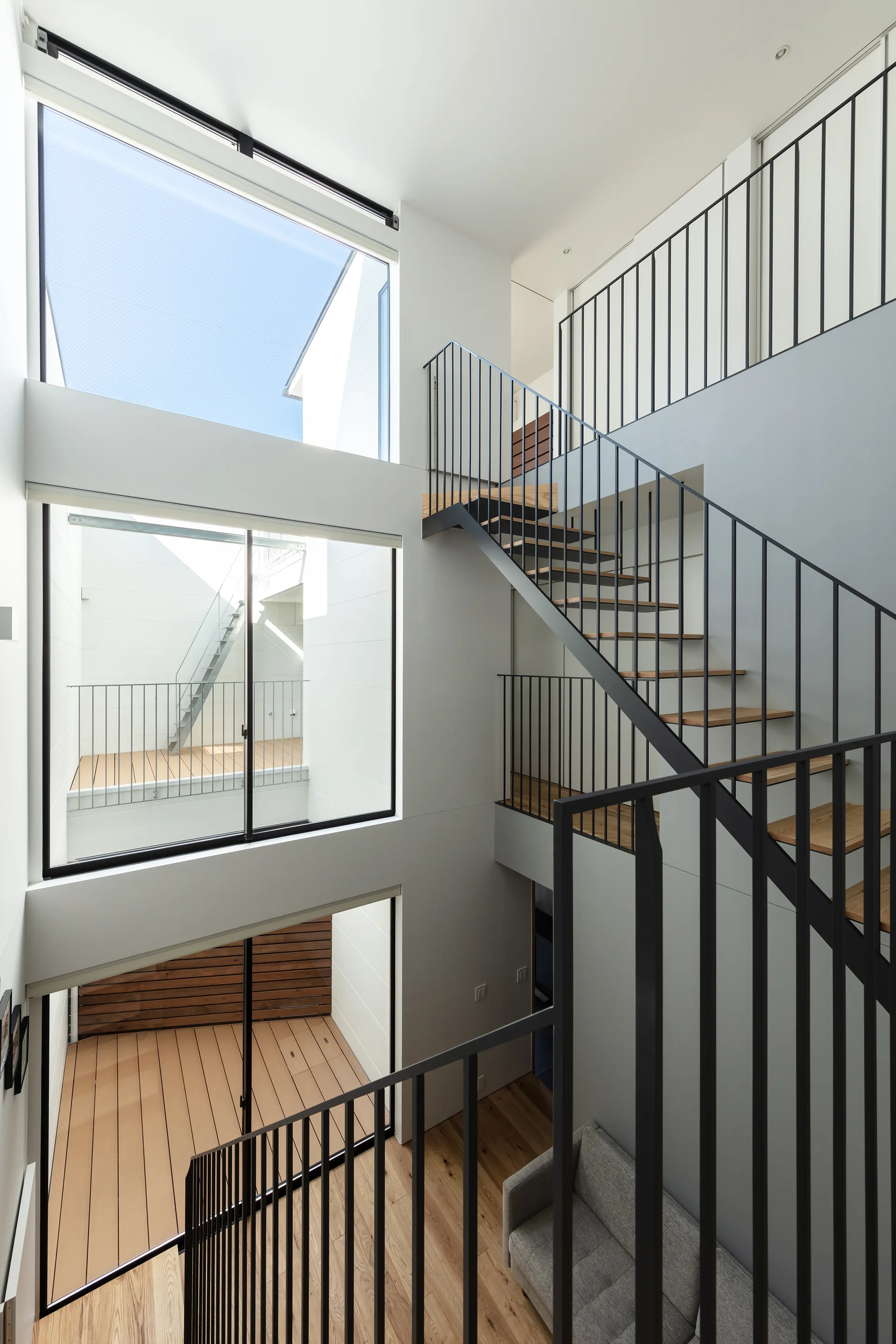 A modern multi-level interior features a black metal open-riser staircase with wood treads alongside large stacked square windows.