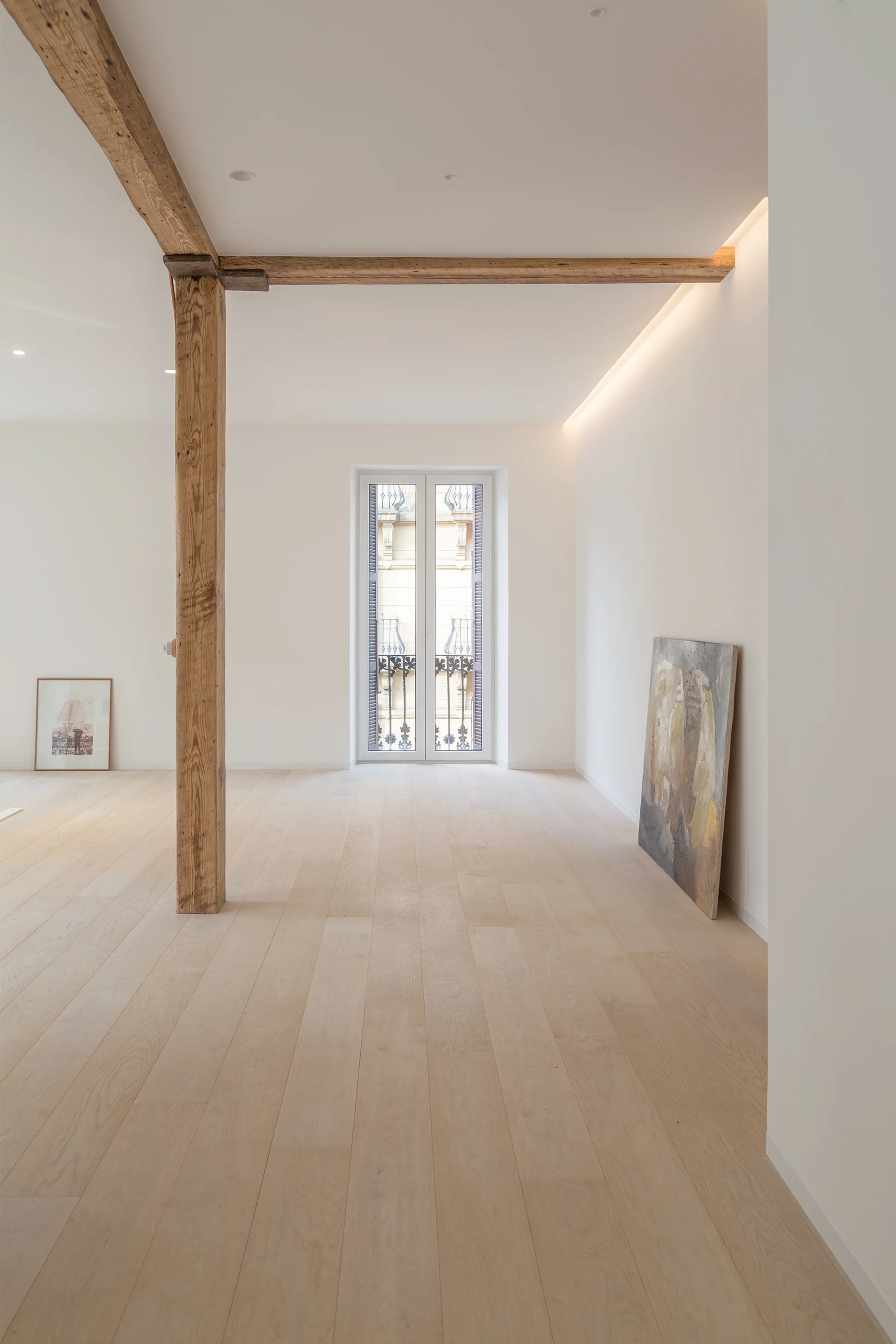 A minimalist room with light wood plank flooring, white walls, an exposed timber support post, and soft cove lighting along the ceiling.
