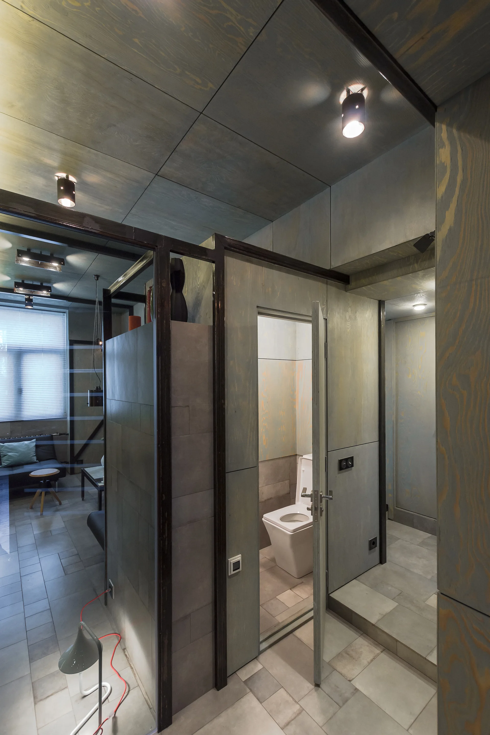 A bathroom featuring grey-stained plywood paneling on the walls and ceiling with a white toilet visible through an open door.