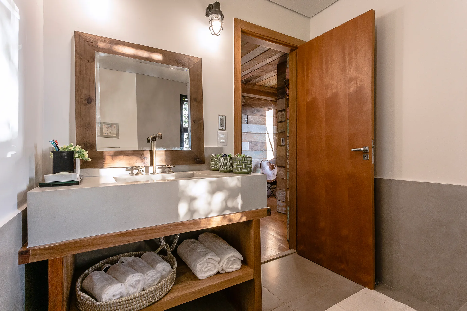 A rustic bathroom features a stone-like concrete vanity with an integrated sink, a large wooden framed mirror, and rolled towels on an open shelf.