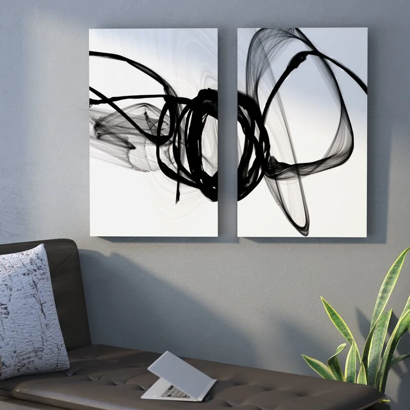 Two black and white abstract art panels hang on a grey wall above a dark tufted leather sofa with a patterned throw pillow.