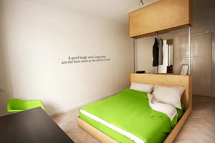 Minimalist bedroom featuring a custom plywood bed structure, bright green bedding, and light herringbone wood floors.