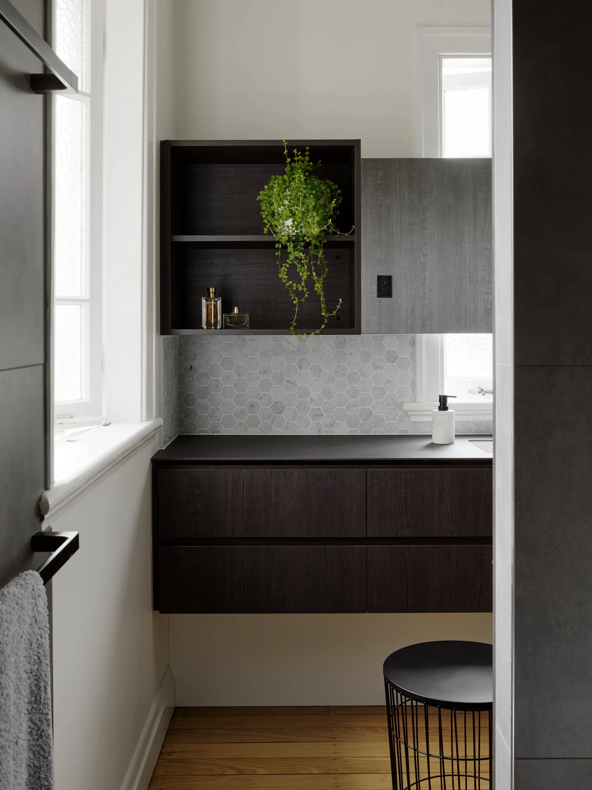 A modern bathroom features a floating dark wood vanity, a marble hexagon tile backsplash, and a wall-mounted open shelf with a trailing green plant.