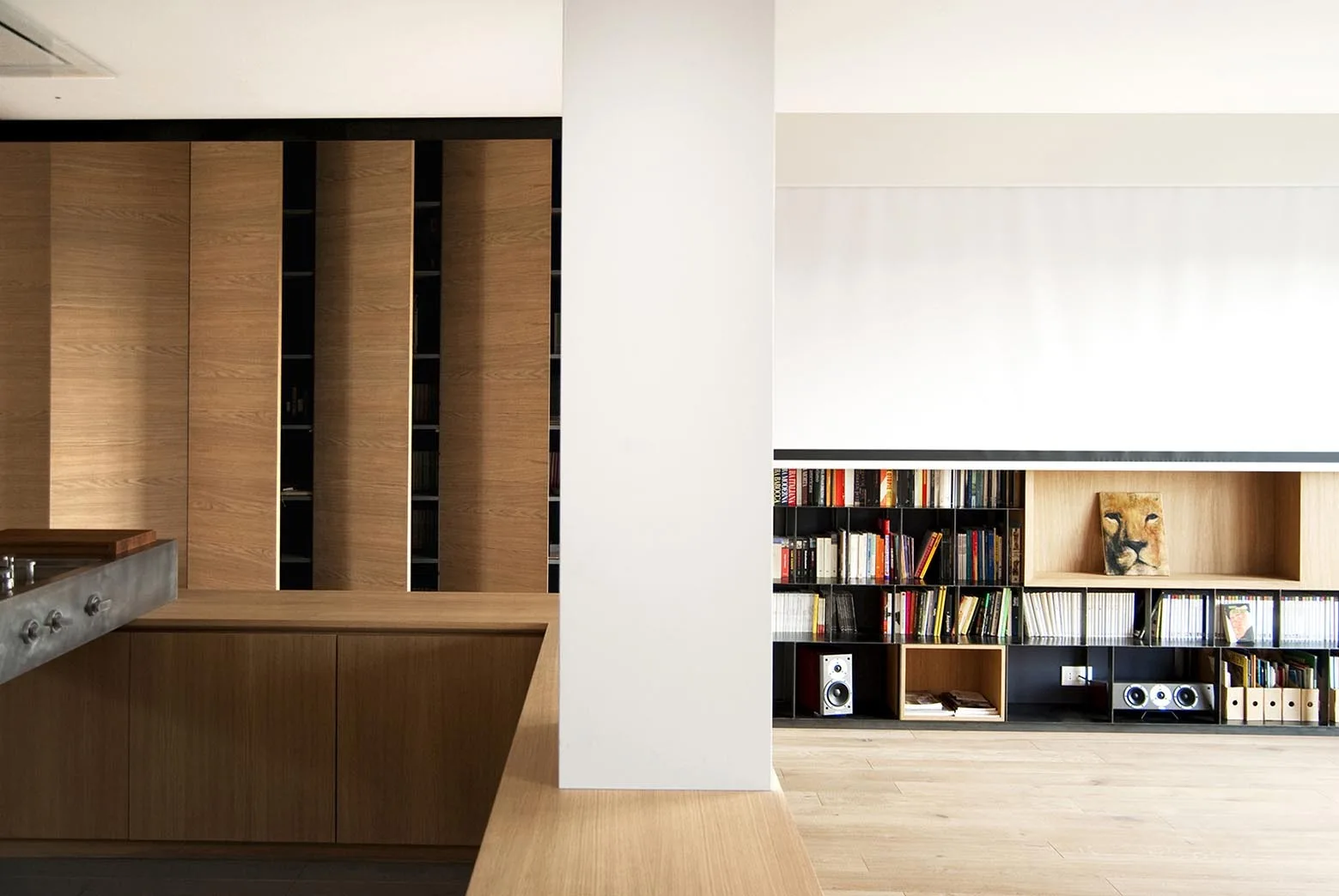 A modern interior featuring vertical wood-toned cabinets, a low built-in metal and wood bookshelf filled with books, and a central white column.