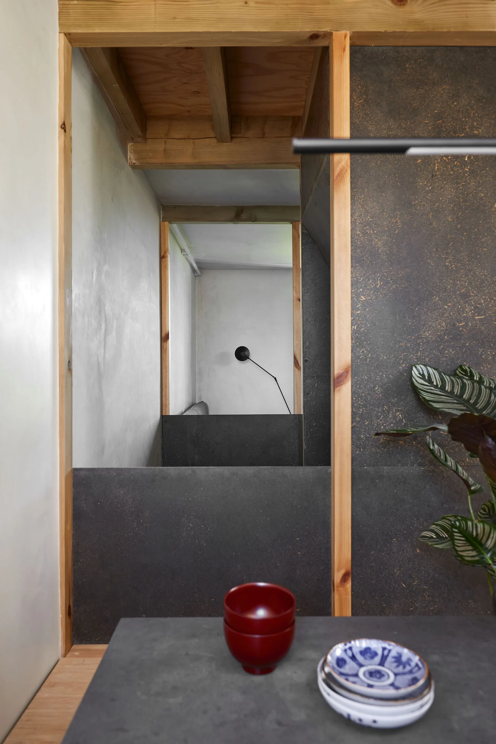 An interior view showing exposed wood framing, matte charcoal wall panels, and small ceramic bowls on a grey tabletop in the foreground.