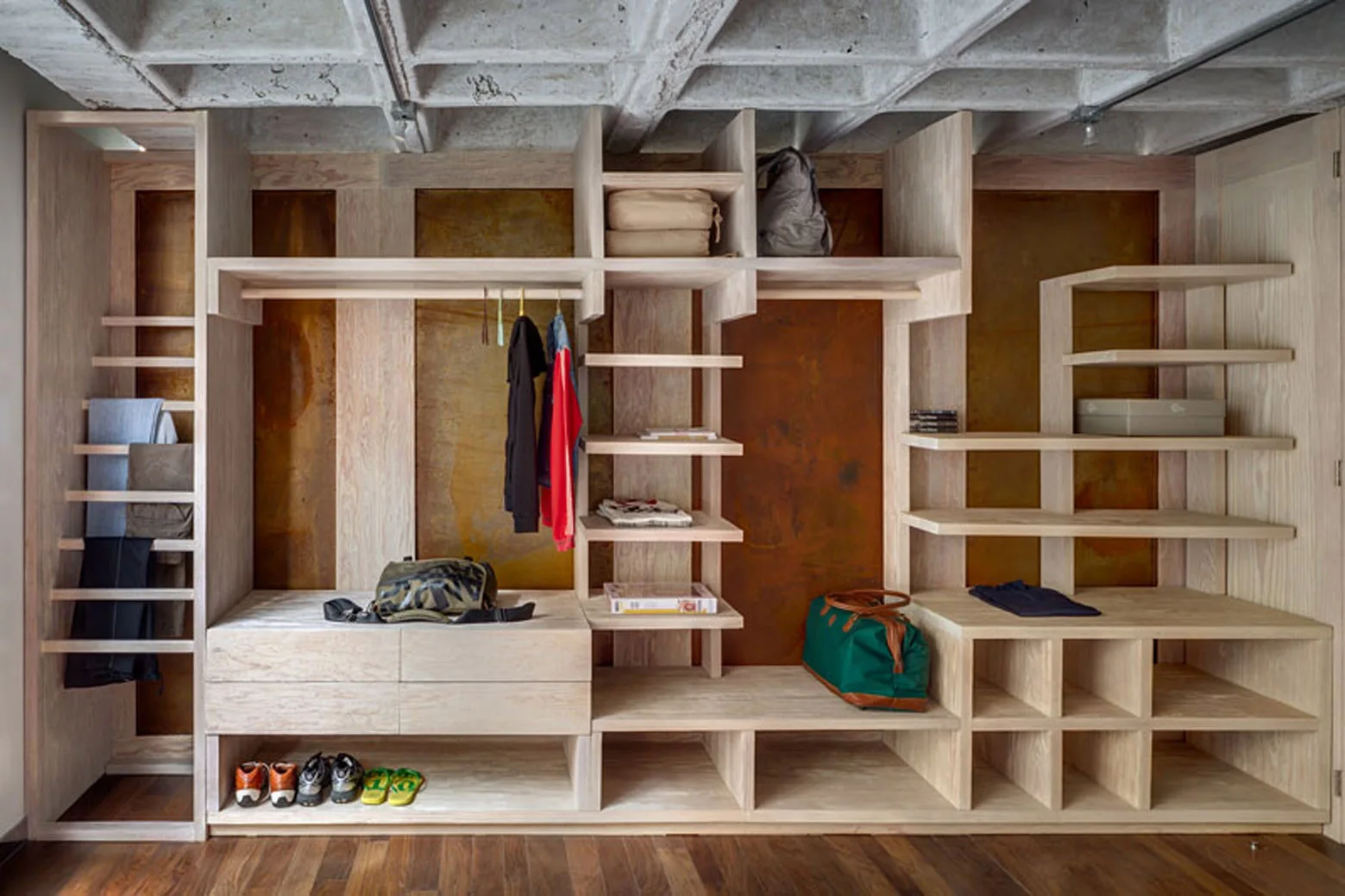 A large built-in light wood shelving unit with open compartments sits against rusted metal wall panels under an exposed concrete waffle ceiling.