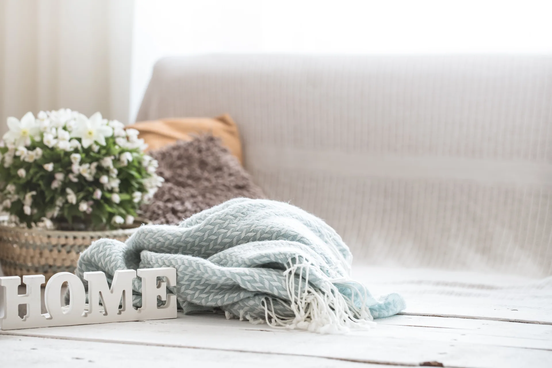 A close-up of a white painted wood table displaying a blue herringbone throw blanket, white wooden letters spelling HOME, and potted flowers.