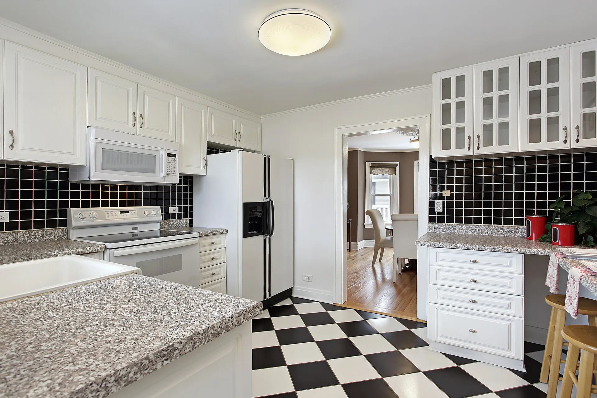 A traditional white kitchen featuring a black tile backsplash, speckled granite countertops, and a black and white checkered floor.