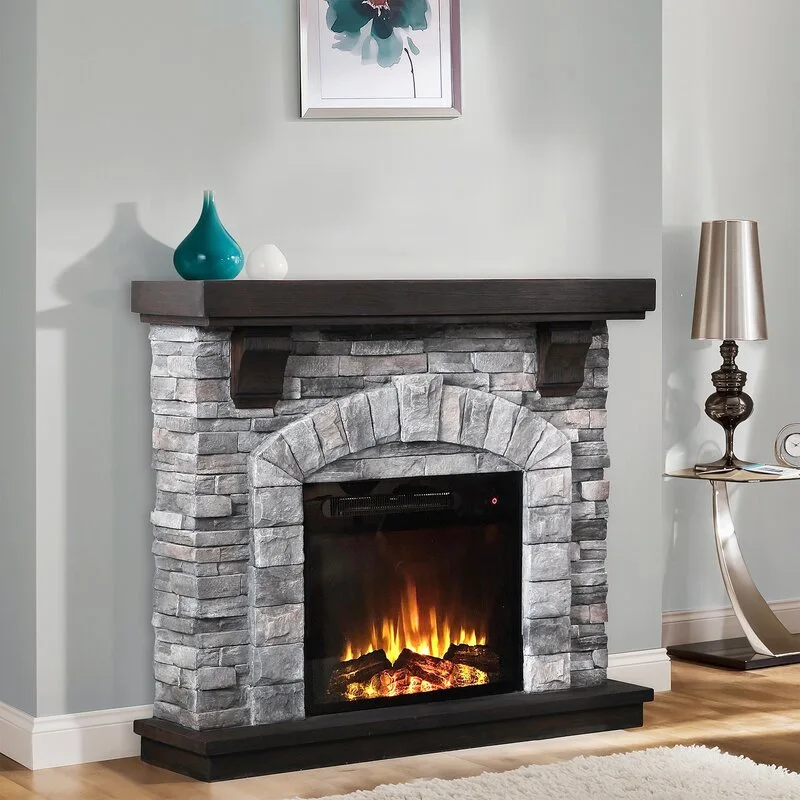 A grey stacked stone electric fireplace with a dark wood mantle and base stands against a light grey wall in a living room.