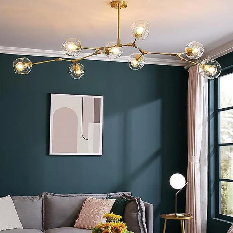 A living room features a branching gold chandelier over a grey sofa, set against a dark teal accent wall with abstract art.