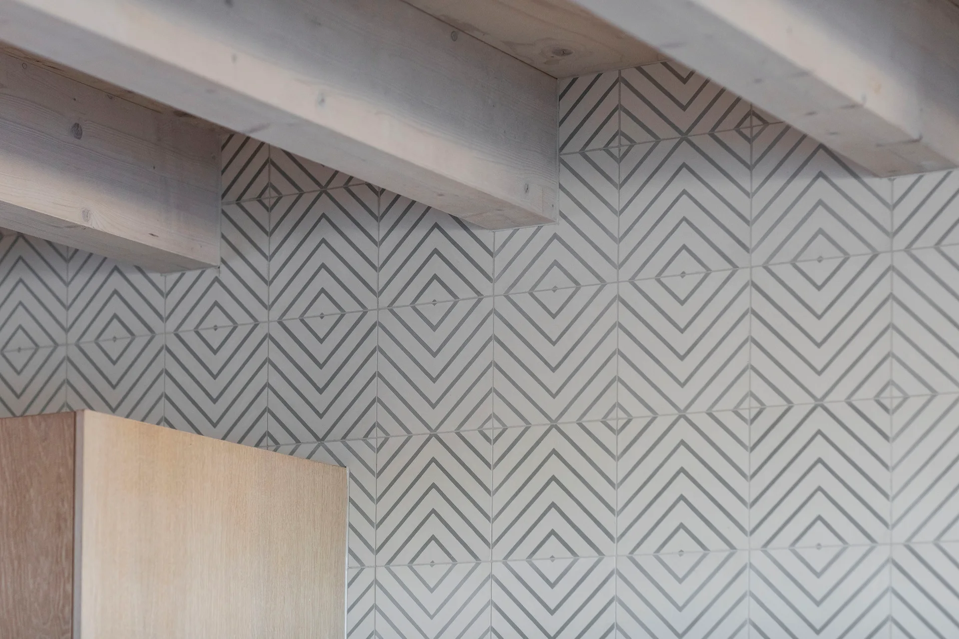 A close-up of grey and white geometric tiled walls underneath exposed light wood ceiling beams.