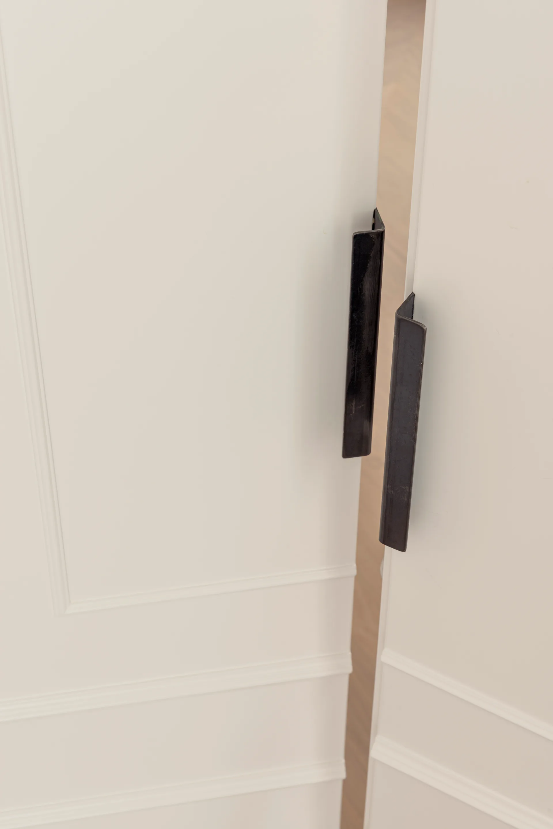Two white paneled doors stand slightly ajar, fitted with slim, vertical black metal edge-pull handles.