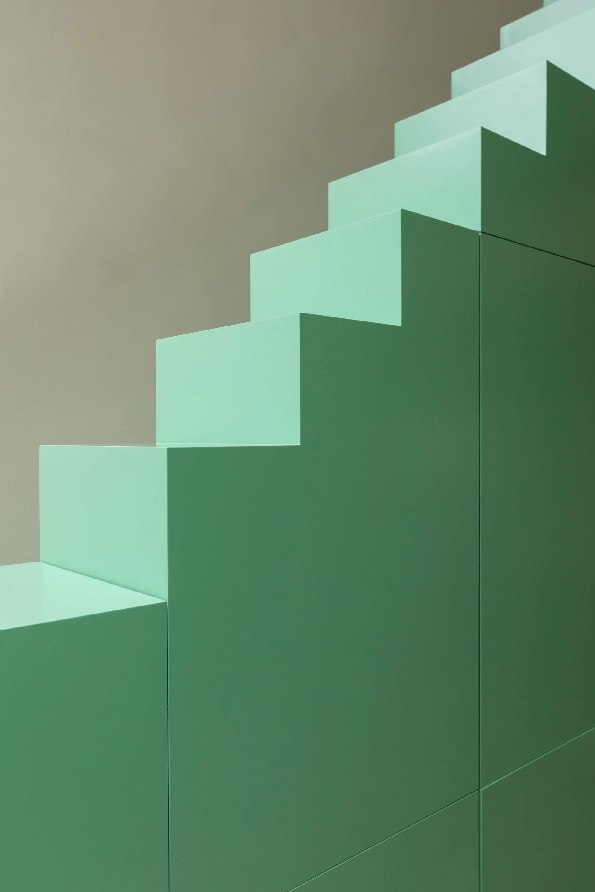 A close-up of a minimalist mint green staircase with blocky geometric steps against a plain grey background.