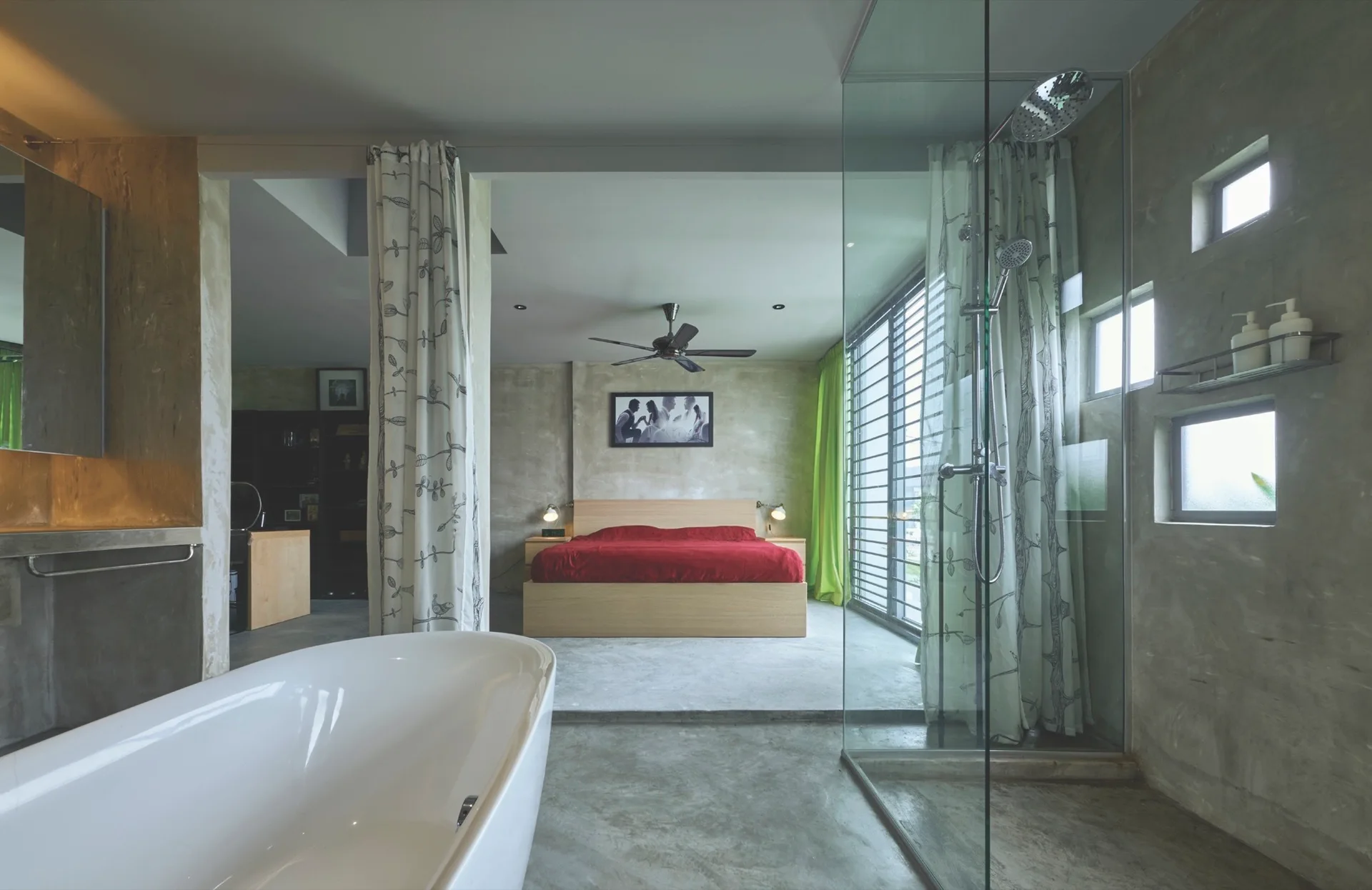 An open-concept bedroom and bathroom features a white freestanding bathtub, a glass-enclosed shower, and a wood platform bed with red bedding.