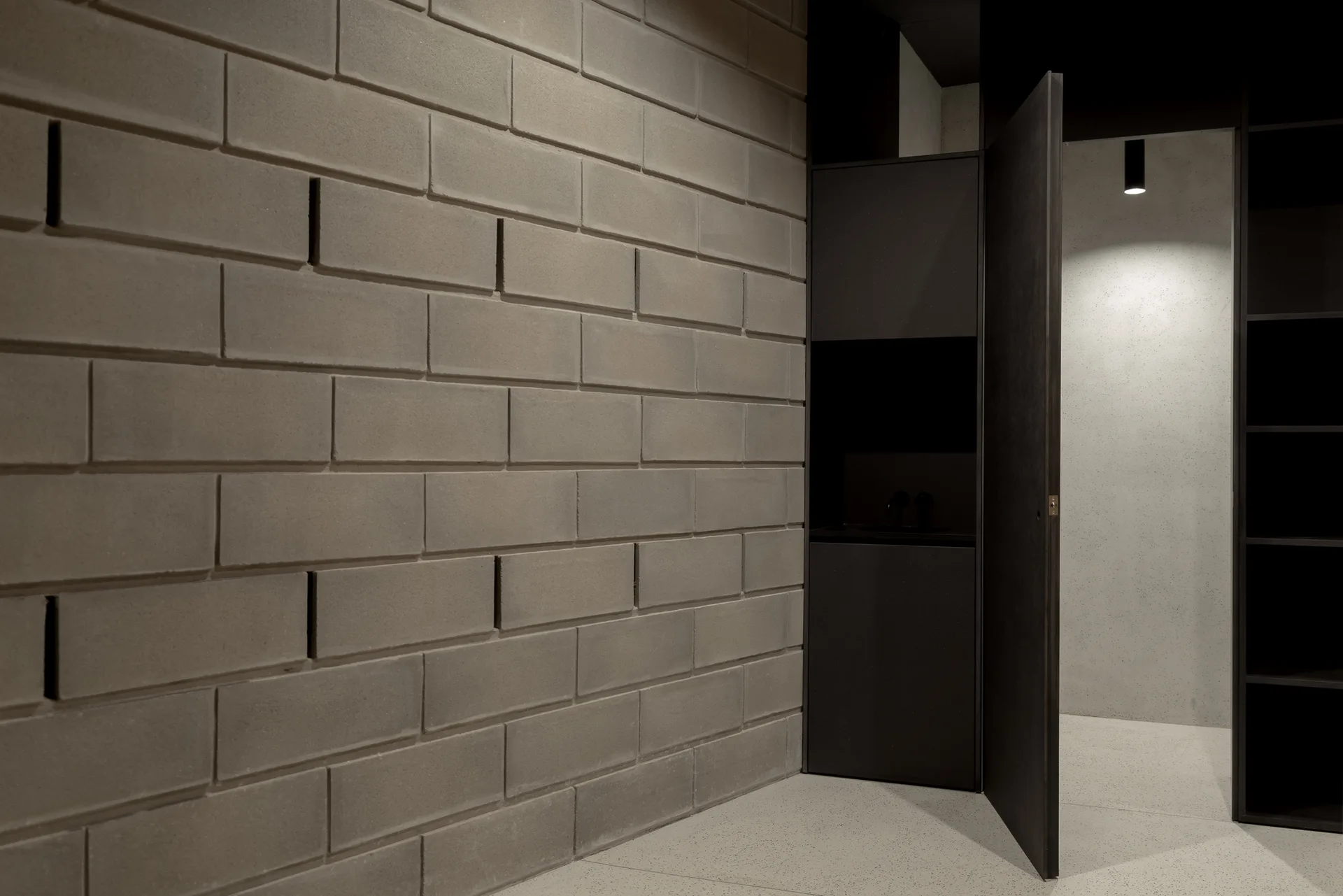 A minimalist room corner featuring a raw grey concrete block wall next to a partially open dark charcoal door.