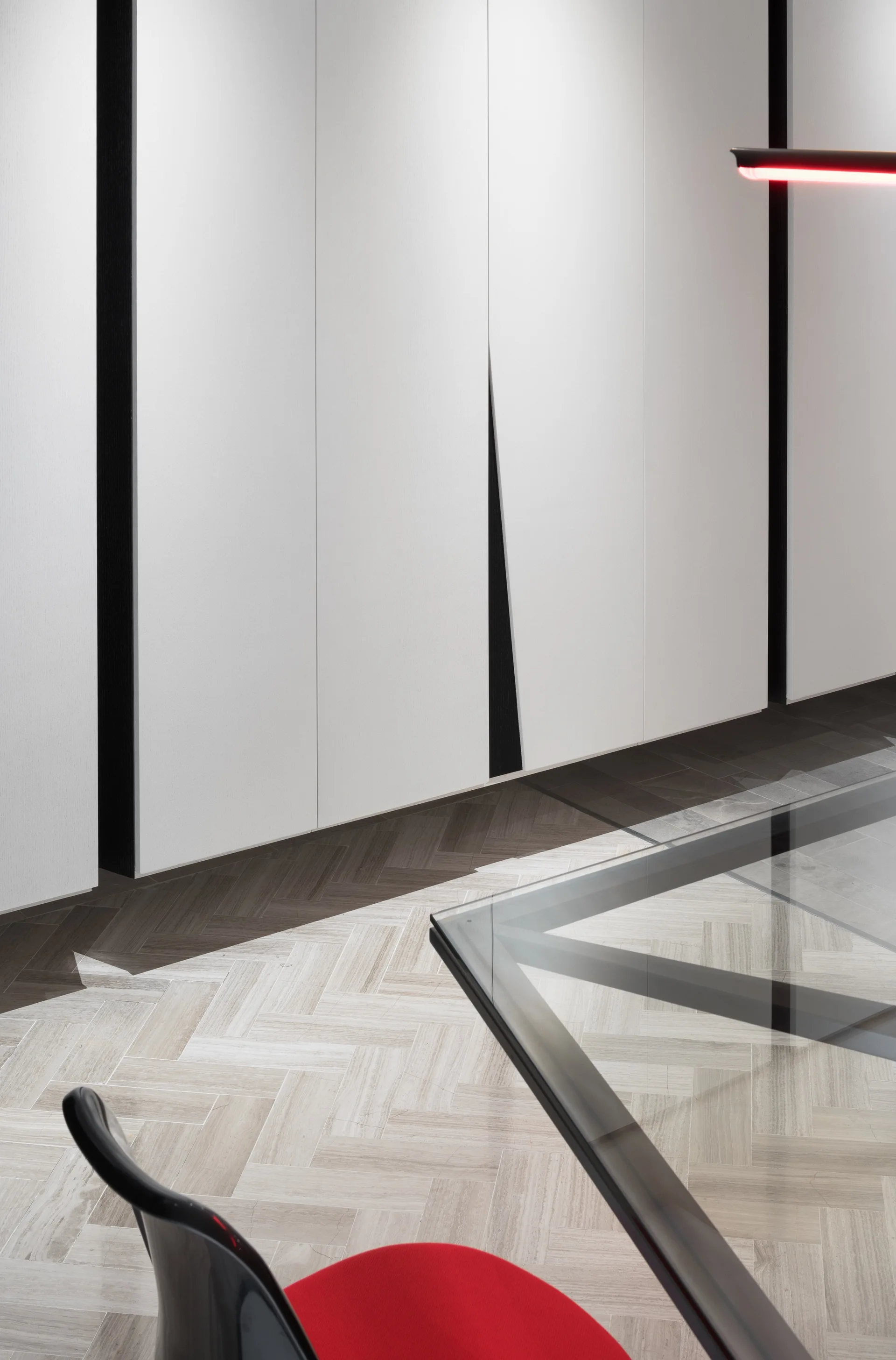 Modern interior detail with floor-to-ceiling white cabinets, contrasting dark wood herringbone floor borders, and a glass dining table.