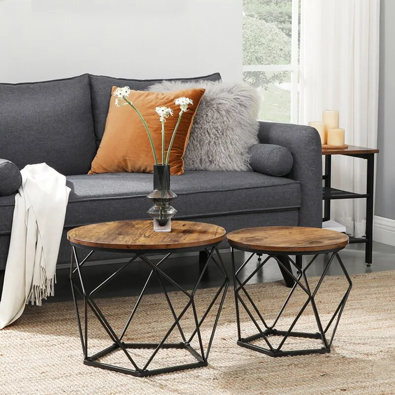 Two round nesting coffee tables with dark wood tops and black wire geometric bases sit in front of a gray sofa on a woven jute rug.
