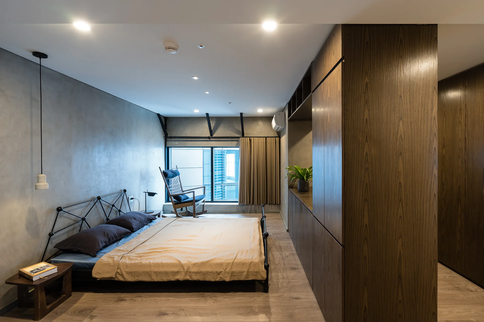 A modern bedroom with textured grey concrete walls, a black metal bed frame, and large wood built-in wardrobes.