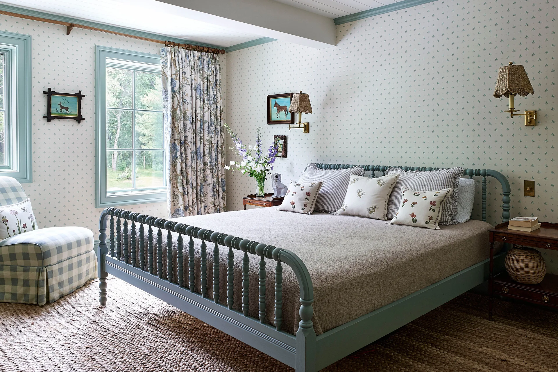 A traditional cottage bedroom featuring a blue-painted spindle bed, small-scale floral wallpaper, and a woven rug.