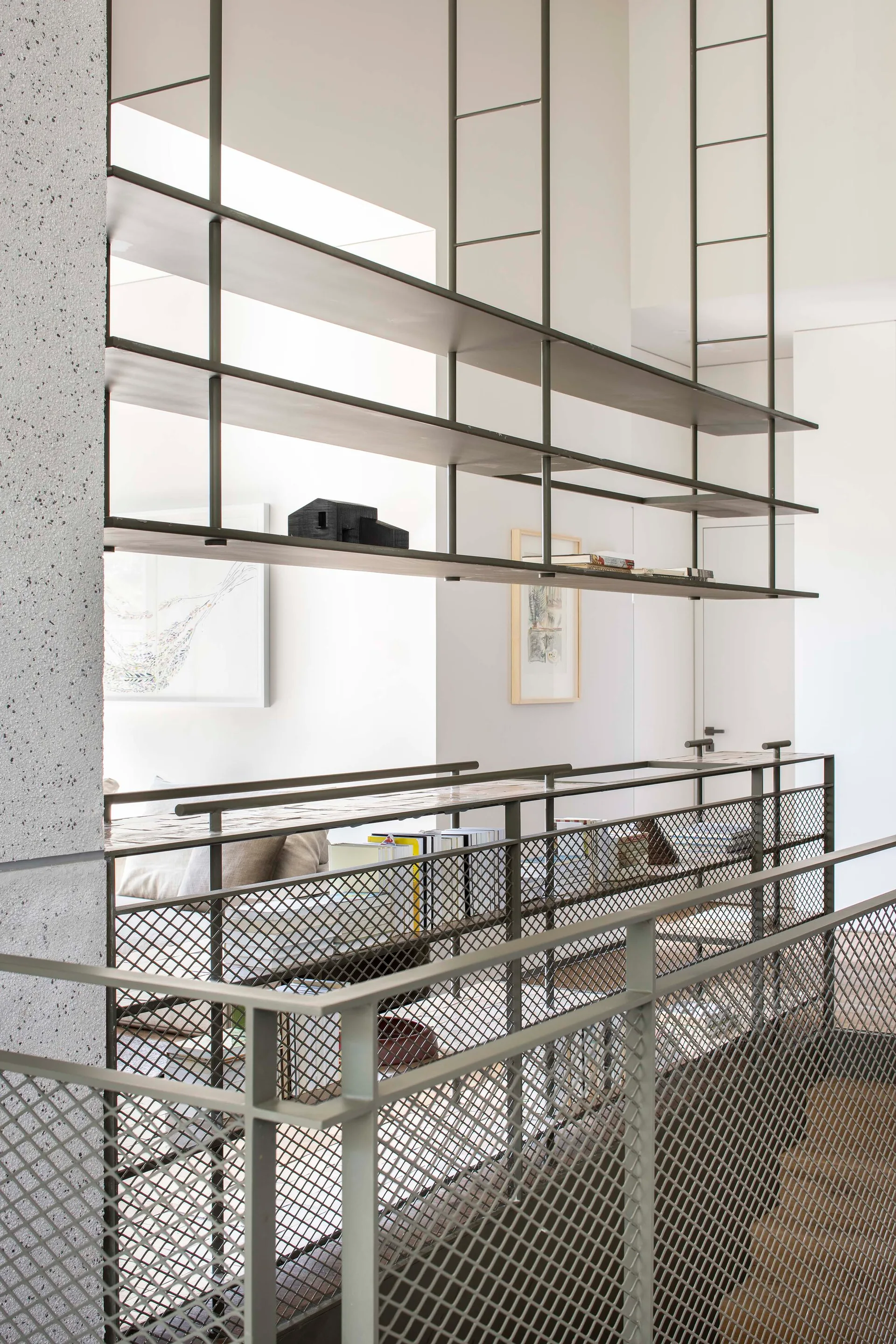 An open home landing features a suspended dark metal shelving unit above a matching metal mesh railing and a concrete structural column.