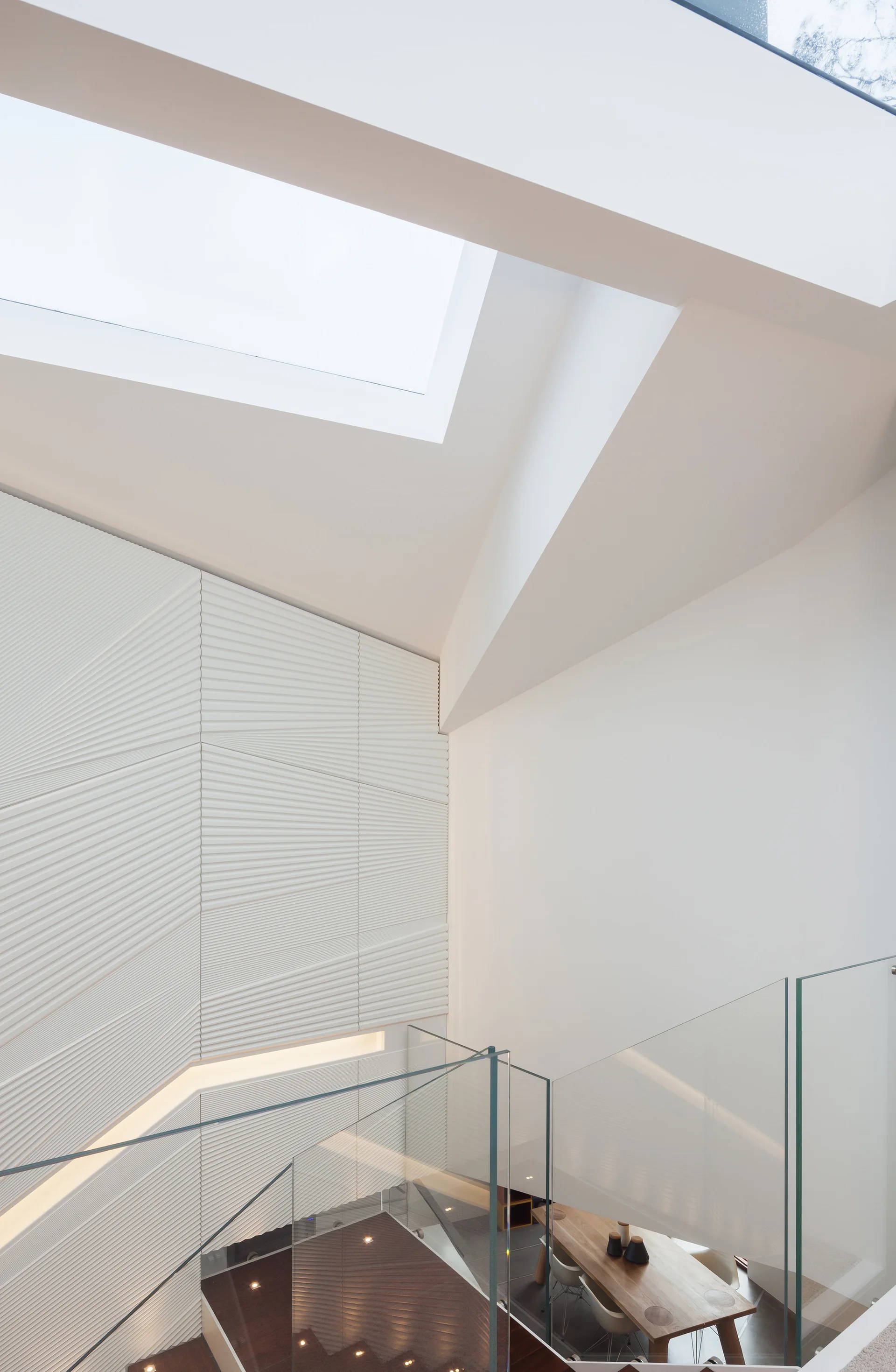 A modern white stairwell features a textured accent wall, a glass railing, and a large overhead skylight illuminating the space.
