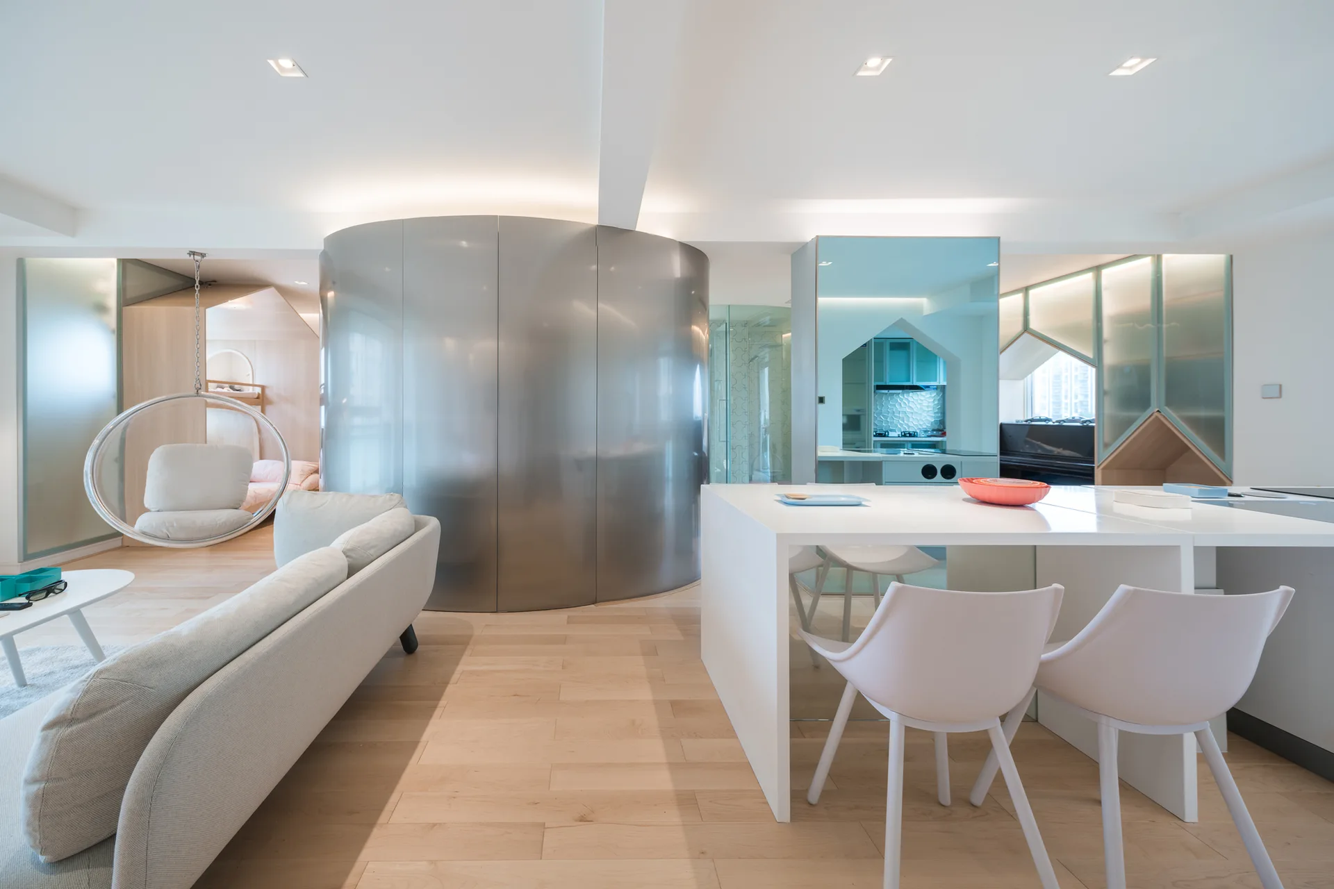 A modern open-plan living room features a large curved metal wall partition, a clear hanging bubble chair, and a white kitchen island.