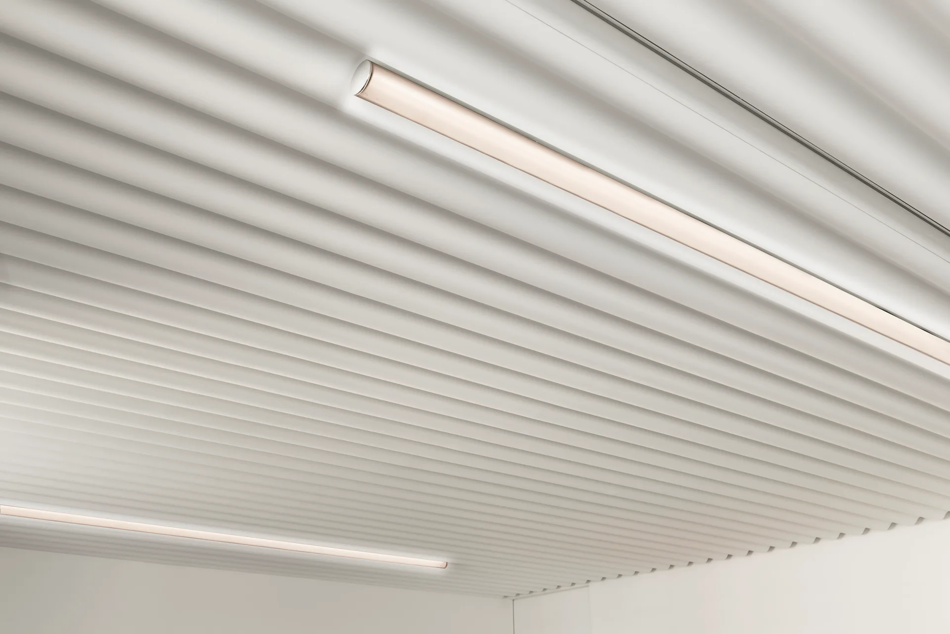 A close-up view of a white ribbed ceiling featuring parallel ridges and recessed linear light fixtures.