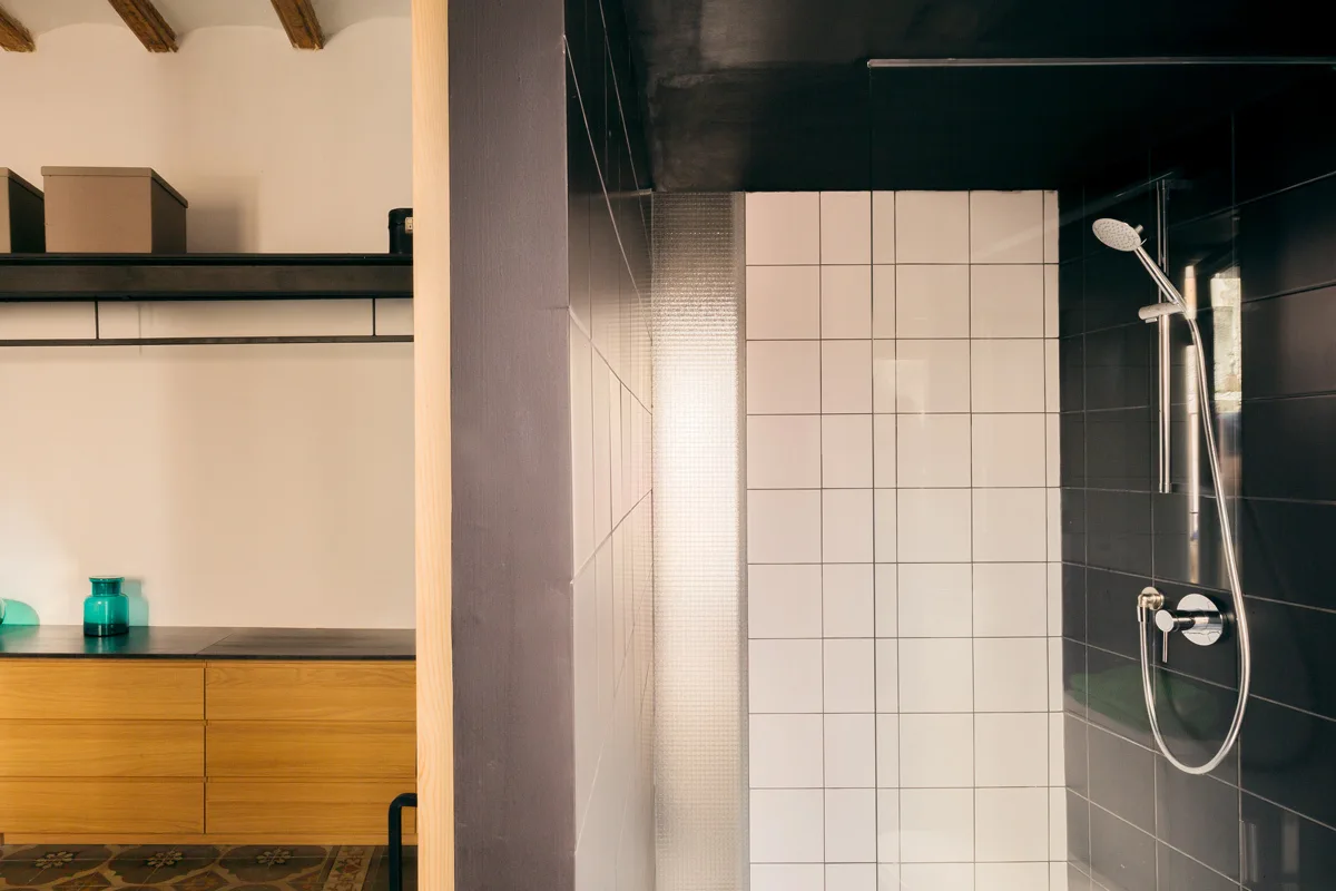 Bathroom featuring a shower stall with black and white grid tiles and a wood-toned vanity set against a dark gray divider wall.