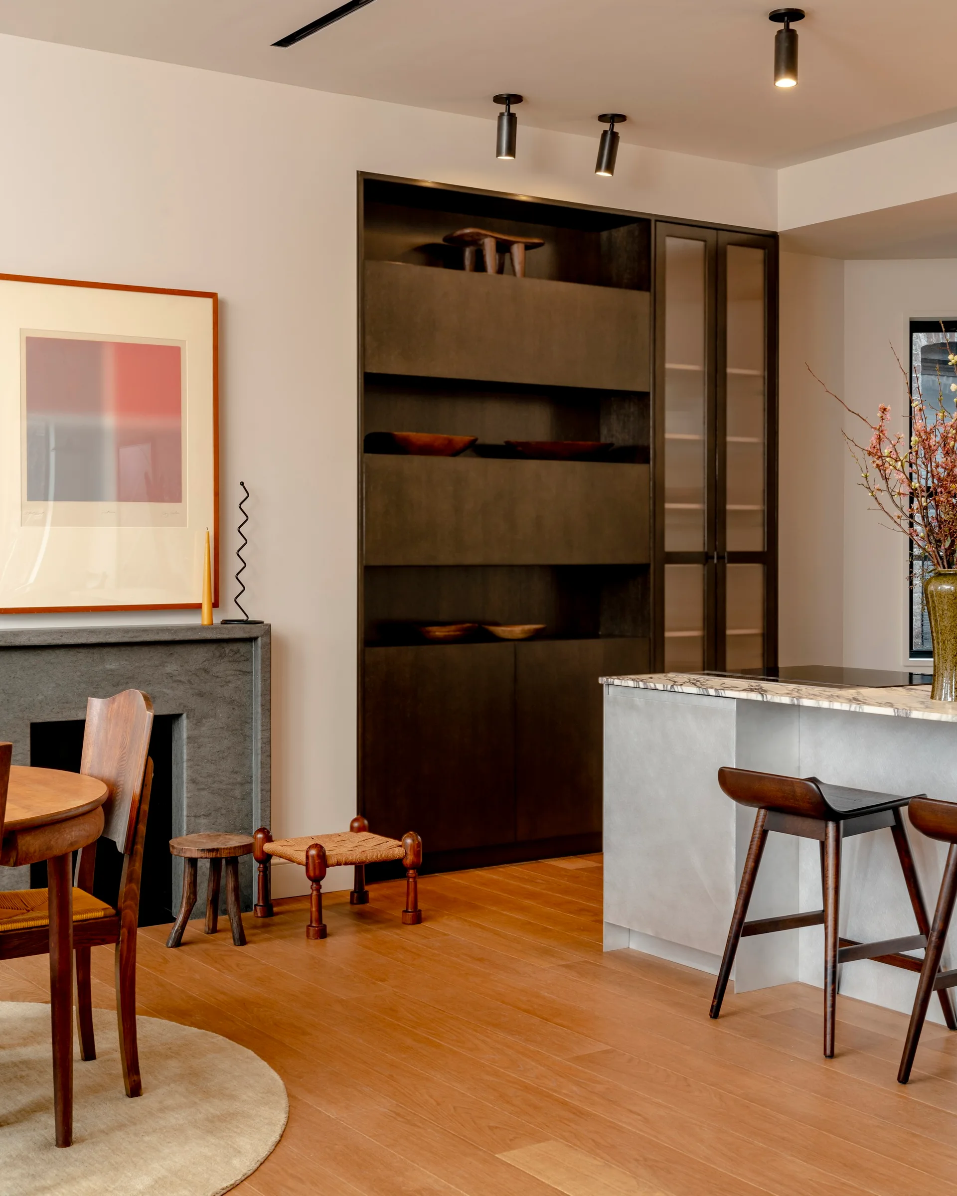 An open-plan kitchen and dining area featuring a marble-topped island, dark built-in cabinets, a stone fireplace, and wood furniture.