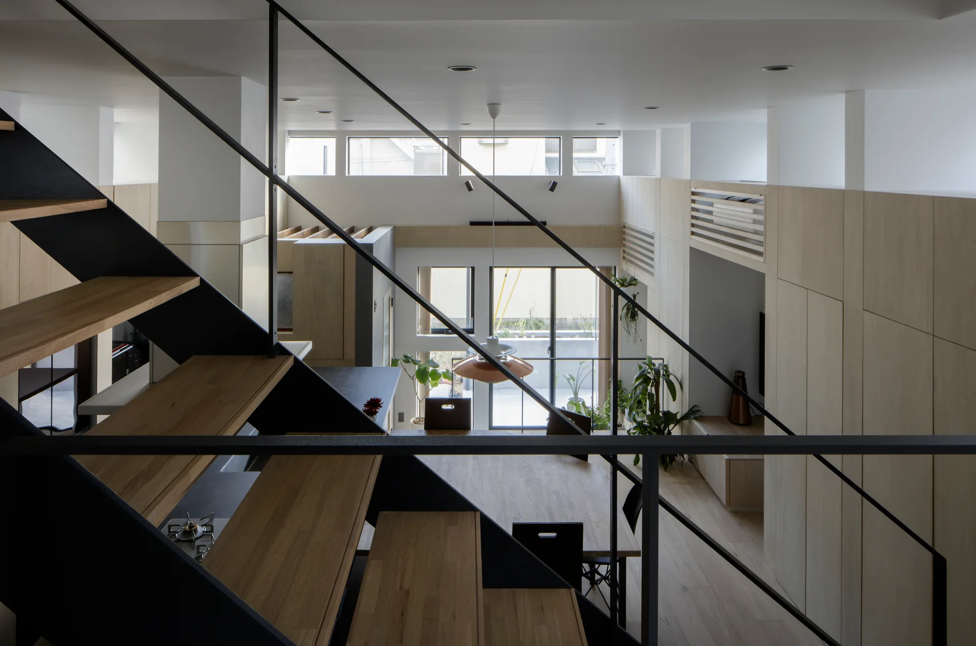 An overhead view from an open-tread wood and black metal staircase looking down onto a dining area with seamless light wood wall cabinets.