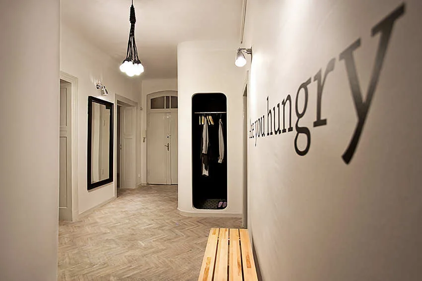 A bright modern hallway featuring light wood herringbone floors, a recessed black closet niche, and a wooden bench.