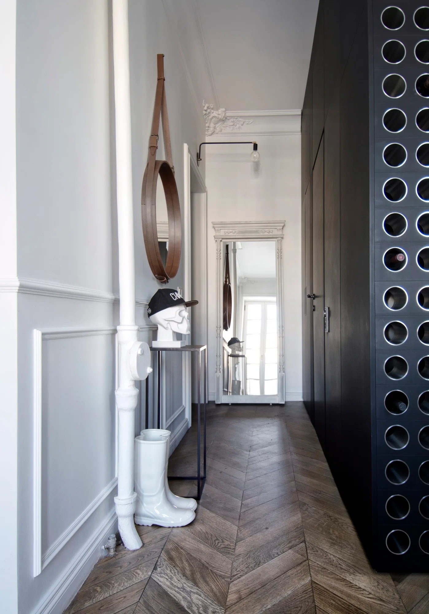 A narrow residential entryway featuring herringbone wood floors, white wainscoting on the wall, and a tall matte black cabinet system.