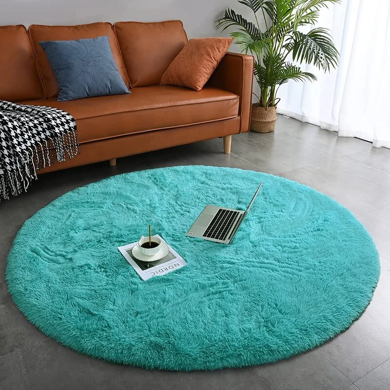 A circular teal shag rug rests on a grey tiled floor next to a brown leather sofa with a patterned blanket and decorative pillows.