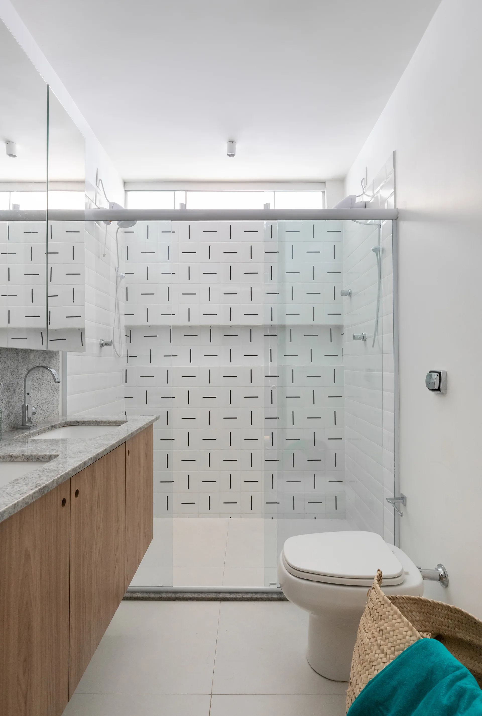A modern bathroom featuring a wood floating vanity, a glass shower enclosure with geometric patterned tiles, and a white toilet.