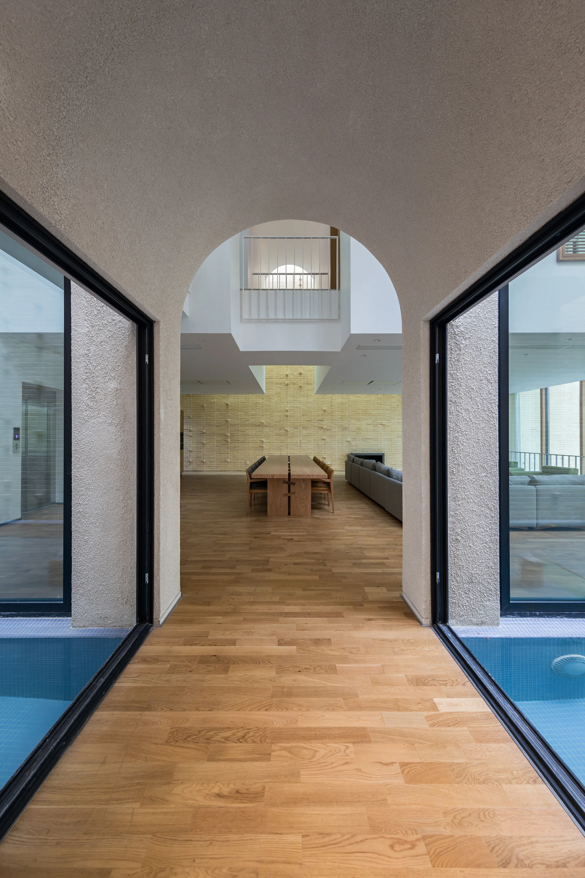 An off-white textured archway frames a long corridor with indoor pools on each side, leading to a spacious dining area with wood floors.