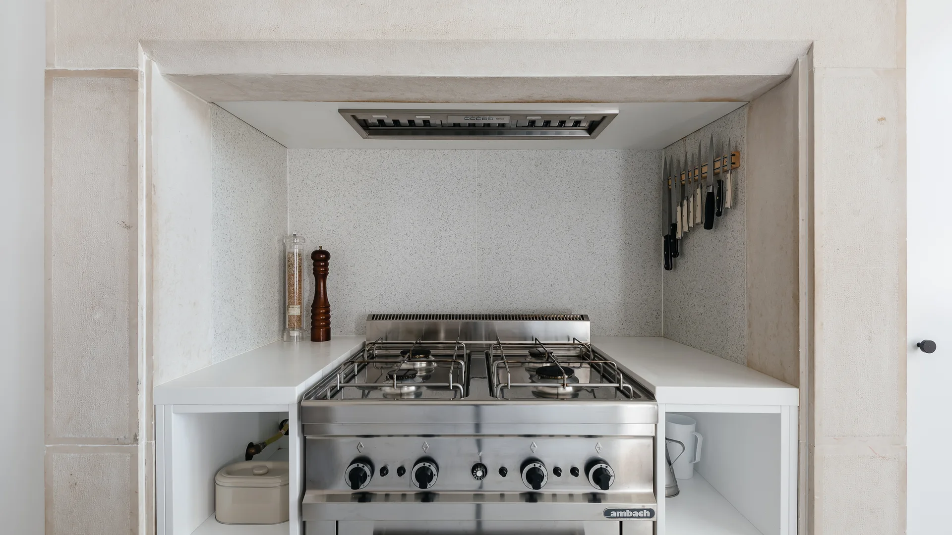 A stainless steel gas range is built into a deep stone alcove with a speckled backsplash and side storage shelves.